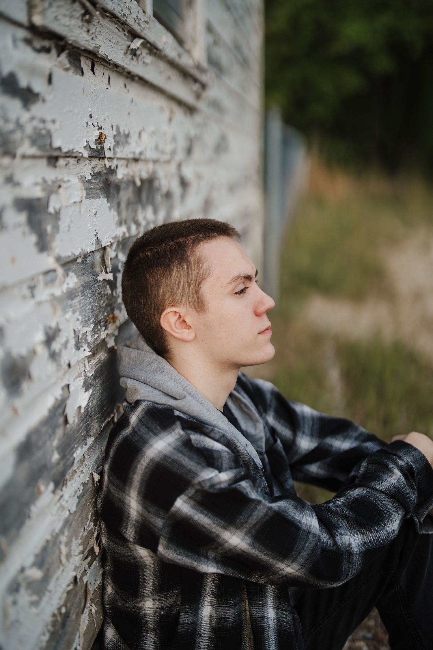 Person in black plaid shirt leans against weathered white wall in outdoor portrait series.