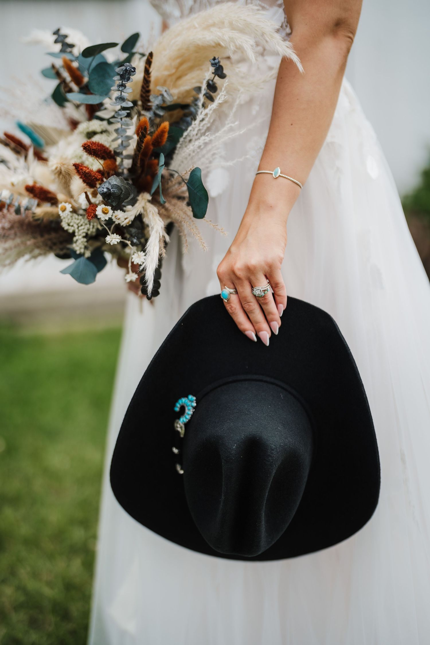 Detail shot of bride holding black cowboy hat with dried flower bouquet.