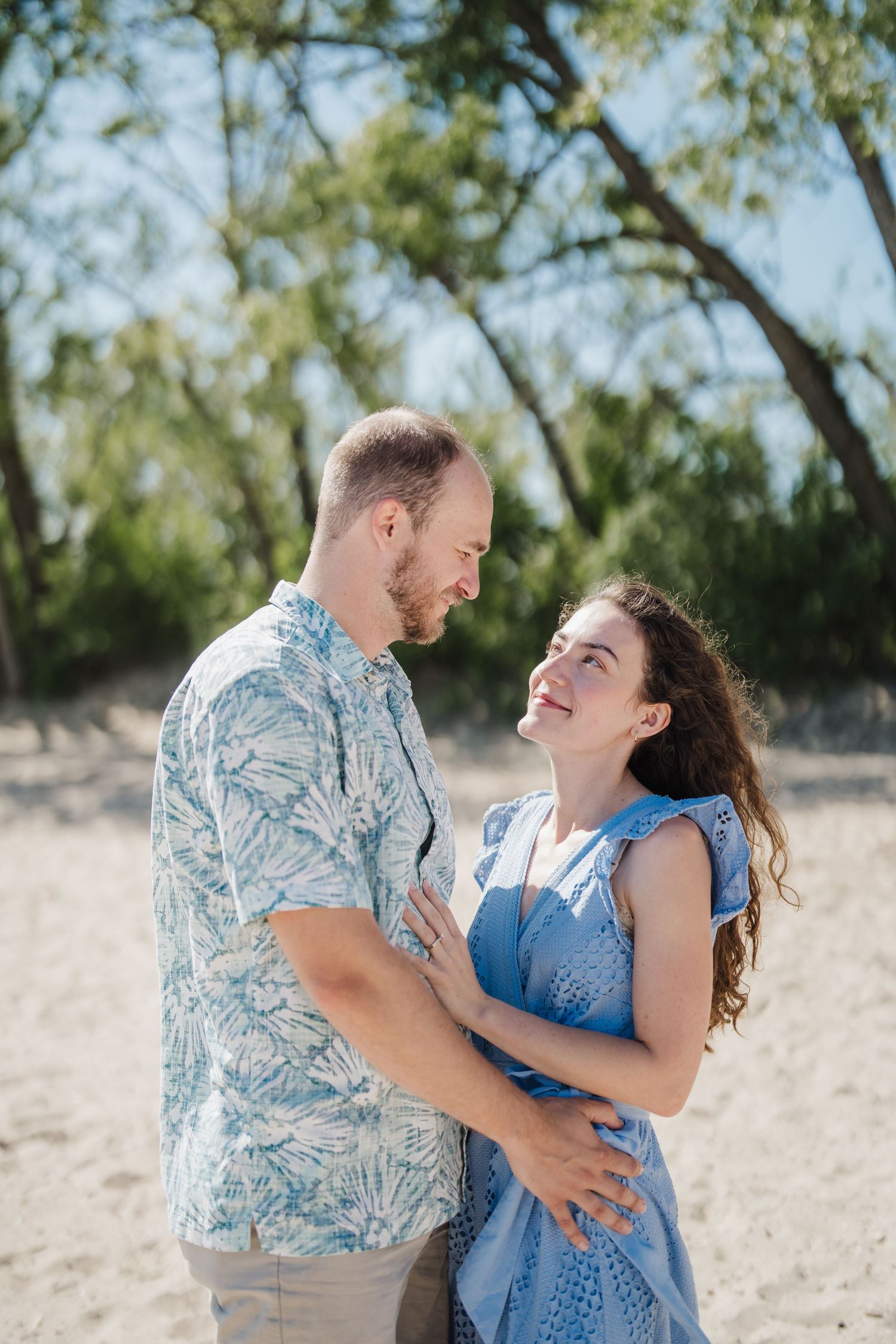 A couple shares joyful laughter together during a romantic outdoor photoshoot in a natural setting.
