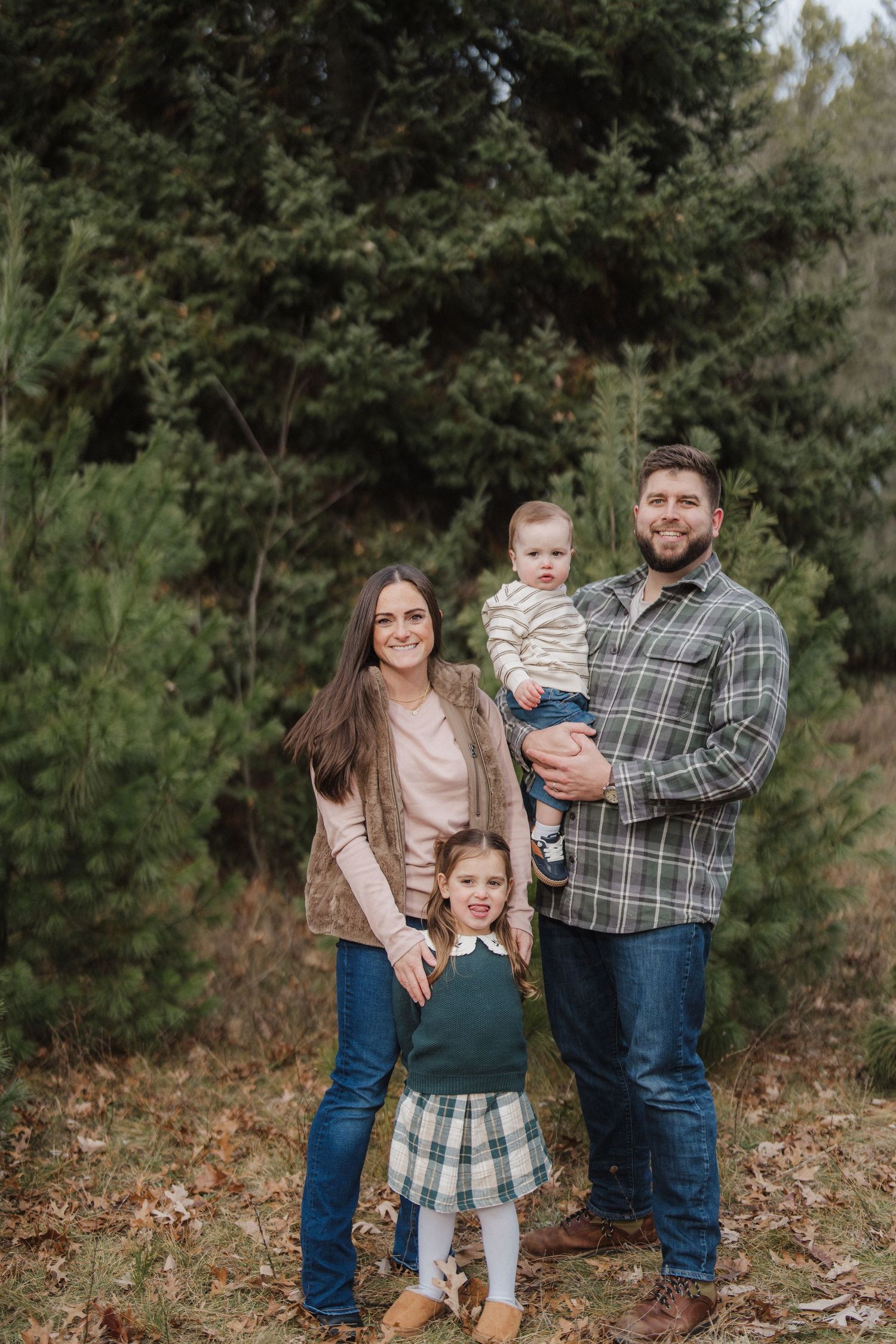 A family poses together in a wooded outdoor setting wearing coordinated casual outfits in autumn.