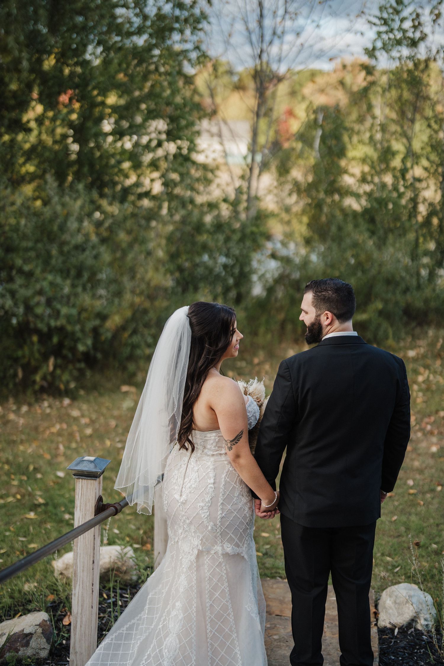 Wedding couple walks hand in hand along a garden path surrounded by autumn foliage.