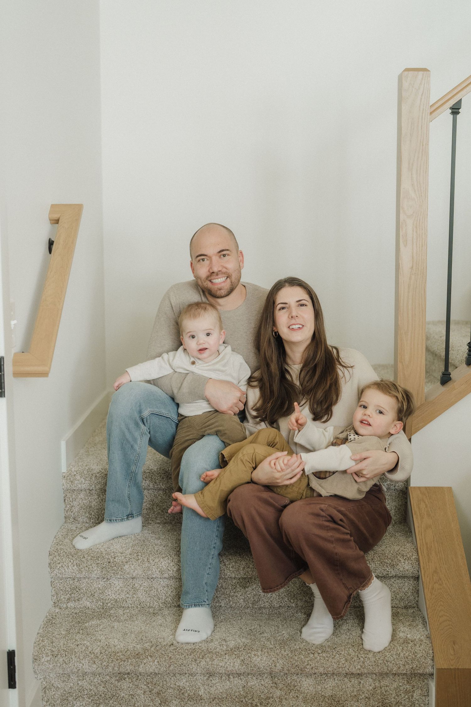 Family sitting together on carpeted stairs in a modern home interior with natural lighting and wooden railings.