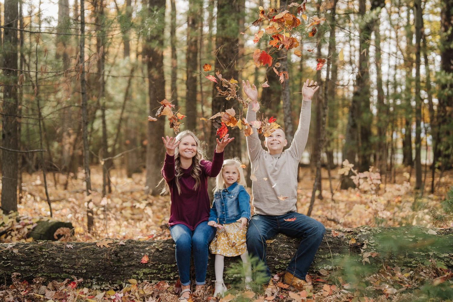 People enjoying a playful autumn moment in the woods as colorful leaves fall around them.