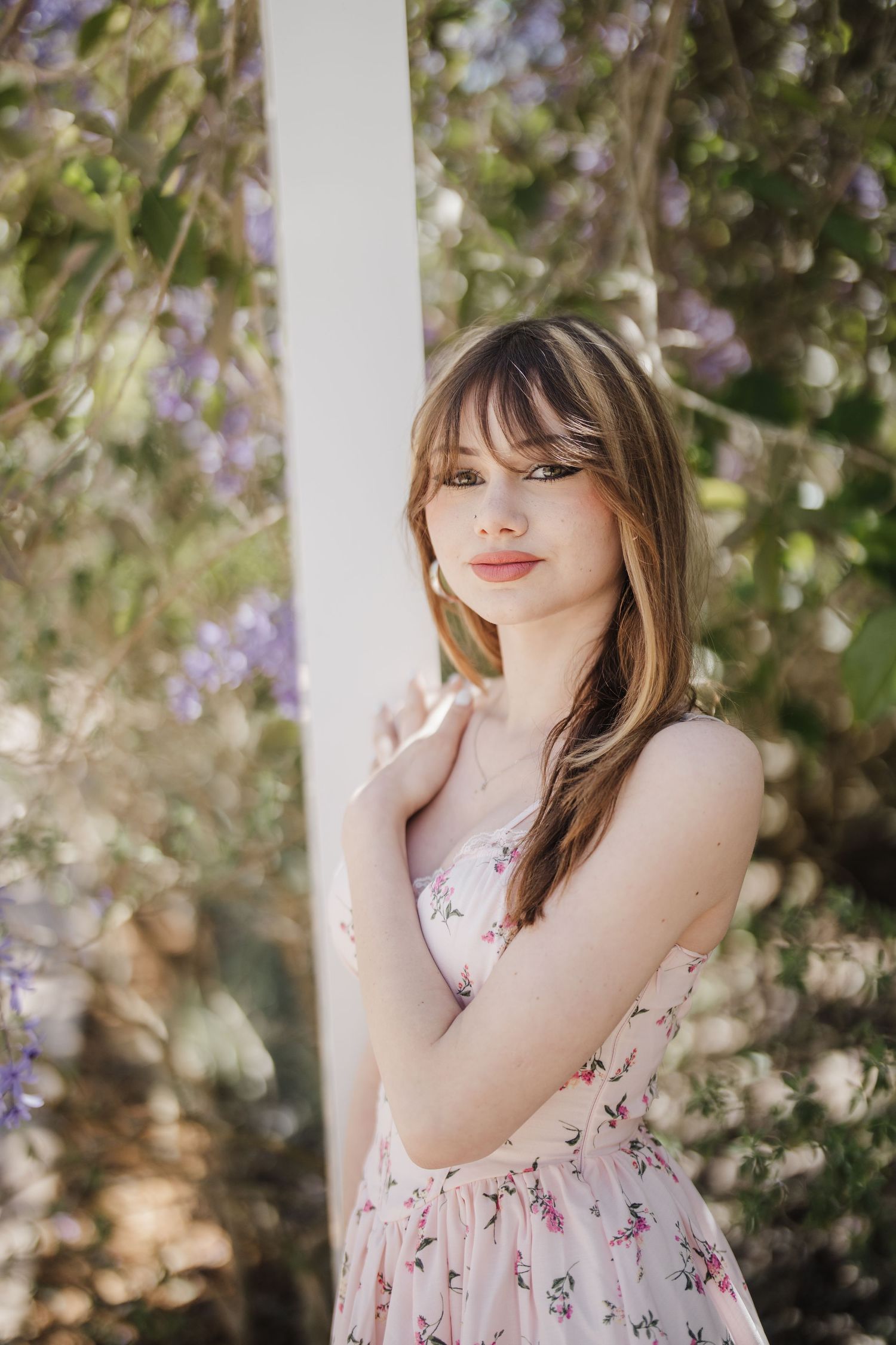 A dreamy spring portrait featuring a floral dress against blooming purple flowers and white columns.