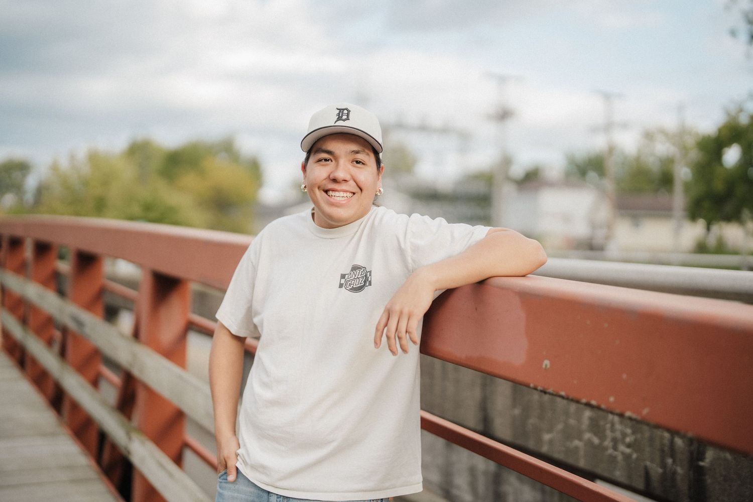 Person in white t-shirt smiling while leaning on red railing with blurred outdoor background.