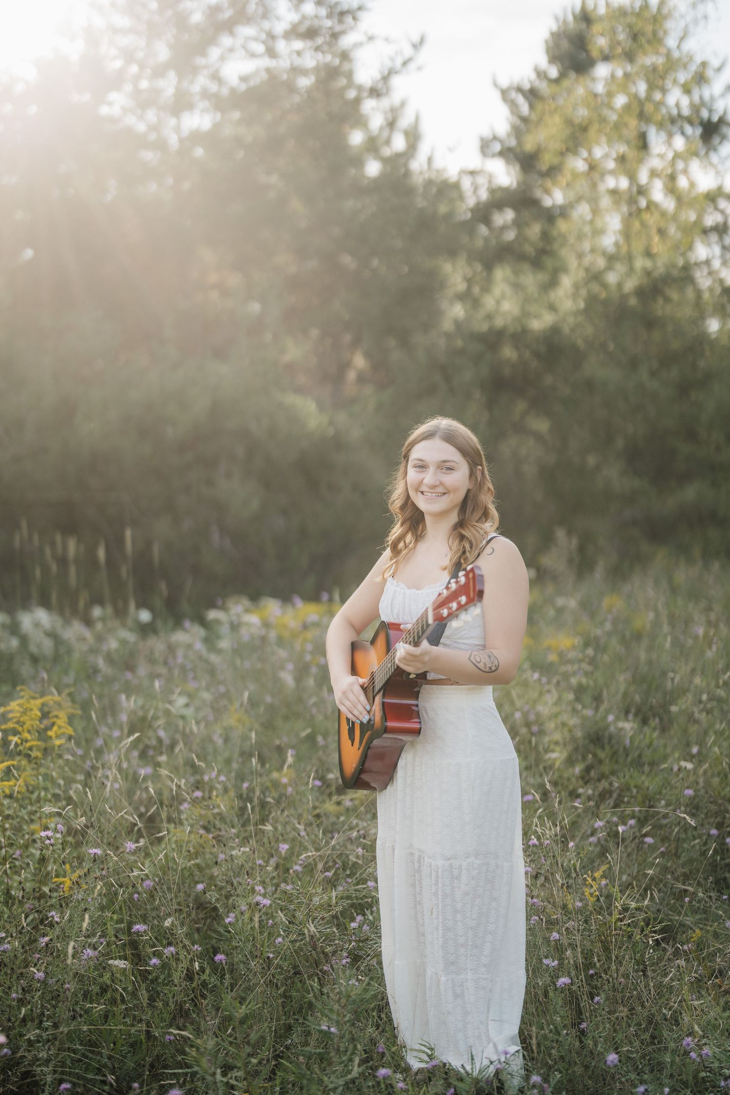 A dreamy outdoor portrait in a wildflower field with a white lace dress and acoustic guitar at golden hour.