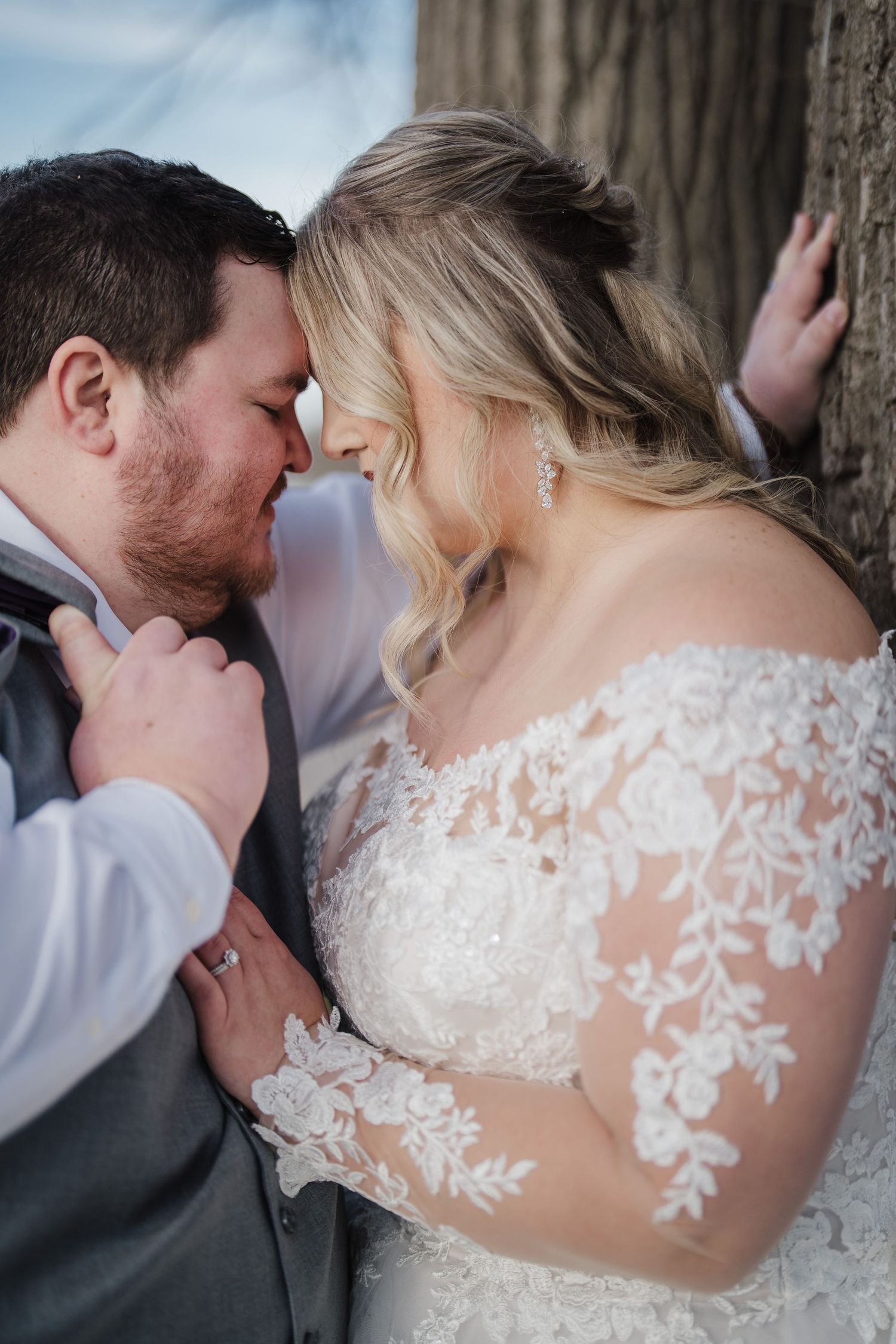 Romantic close-up of newlyweds sharing intimate moment against tree.