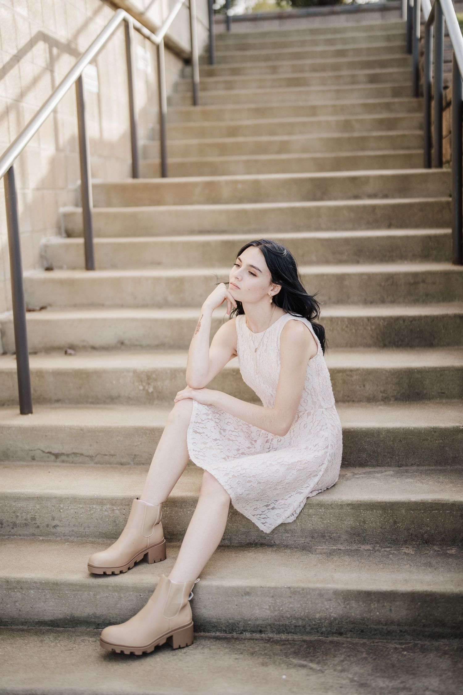 A person in a white lace dress poses gracefully on concrete steps while wearing beige combat boots.