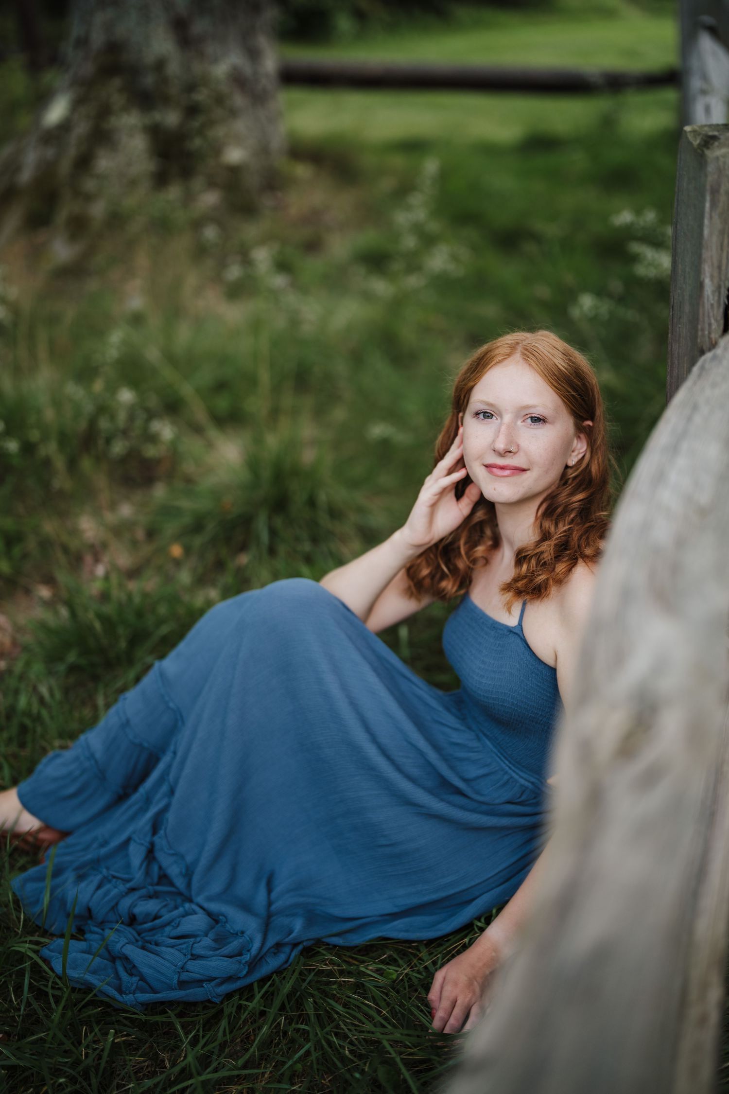 A graceful portrait session features a navy blue dress against a rustic wooden backdrop in a garden setting.