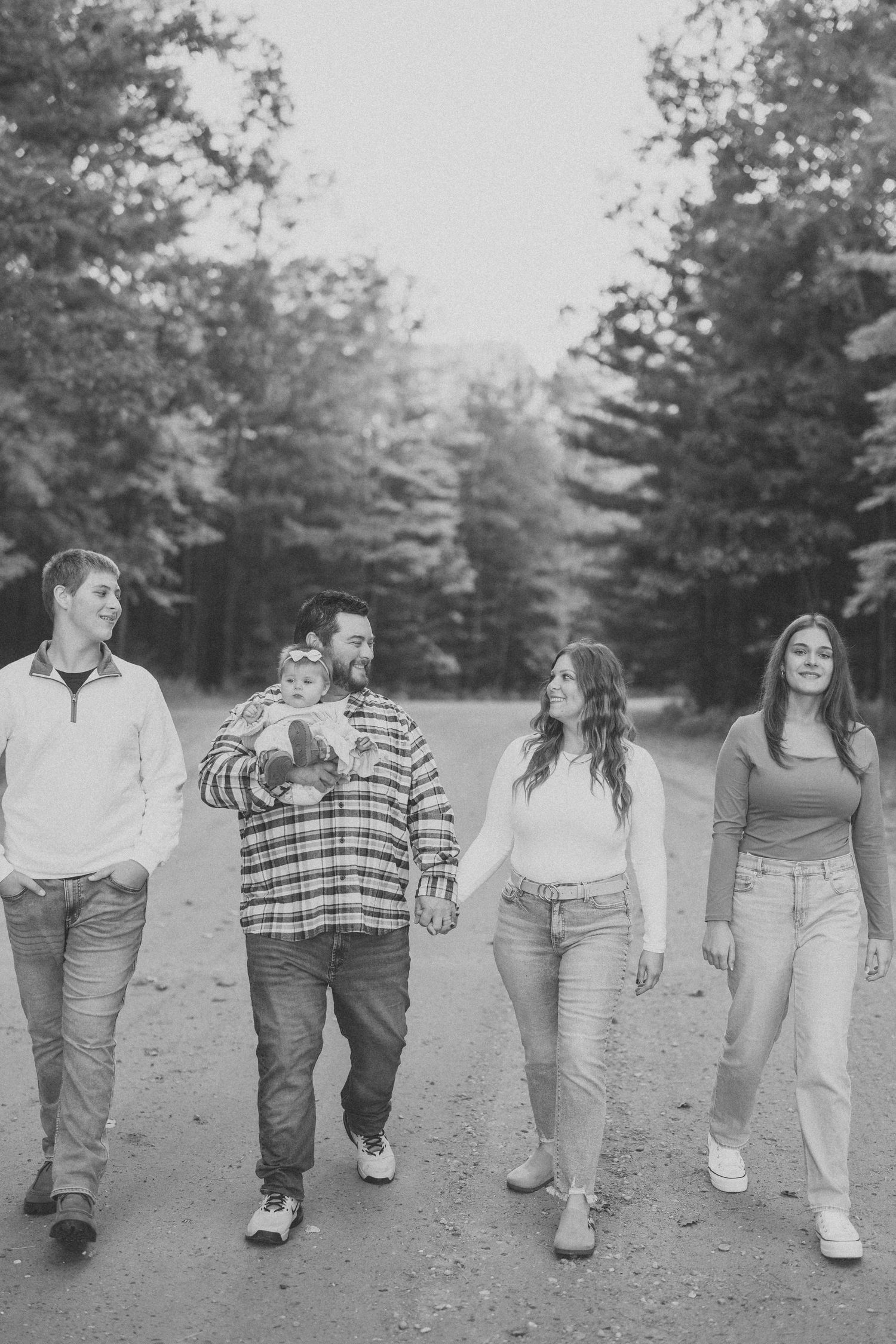 A group of friends in casual attire walking together on a dirt path through a wooded area in black and white.