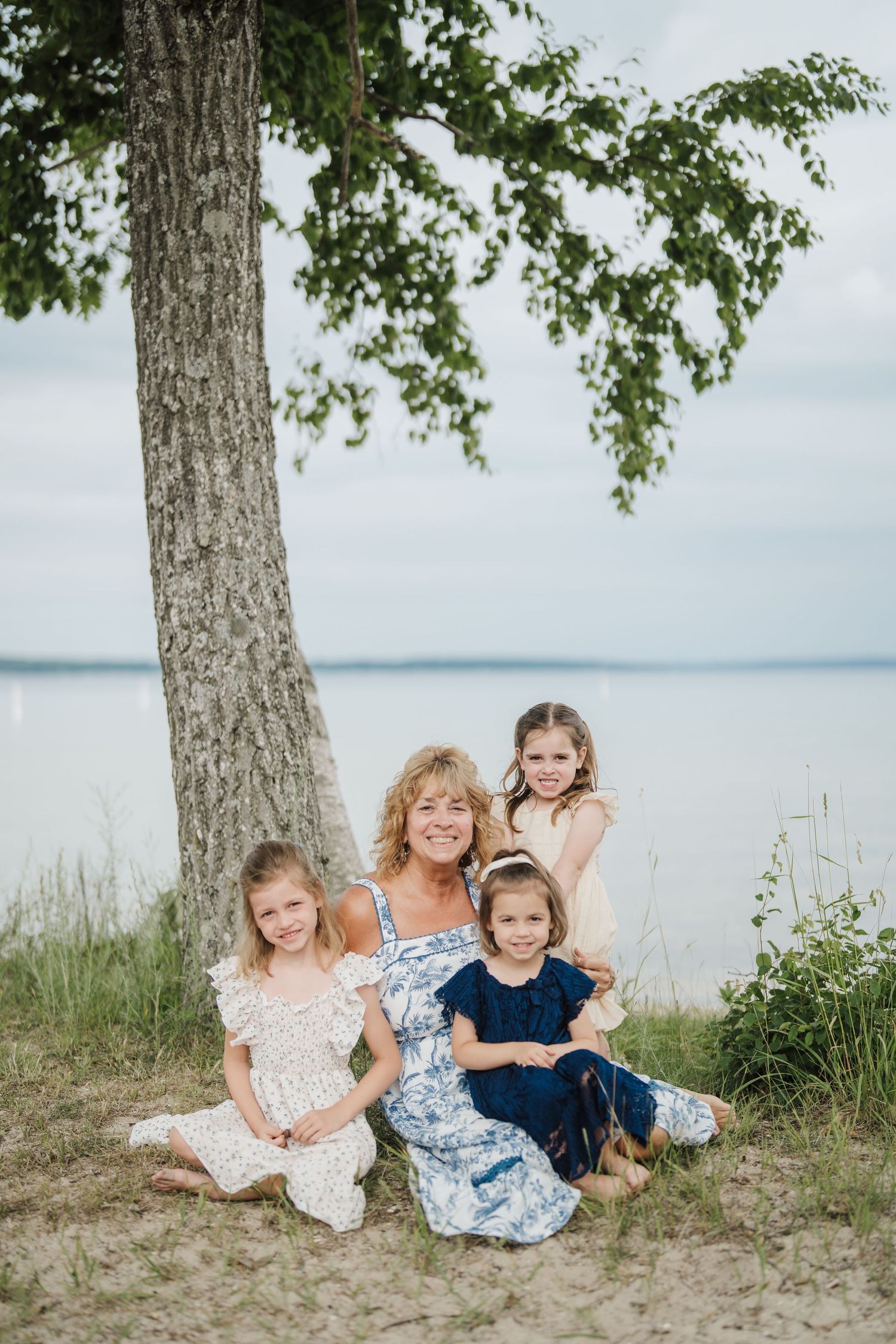Children in coordinating blue and white outfits play and laugh together on a sandy beach near the water.