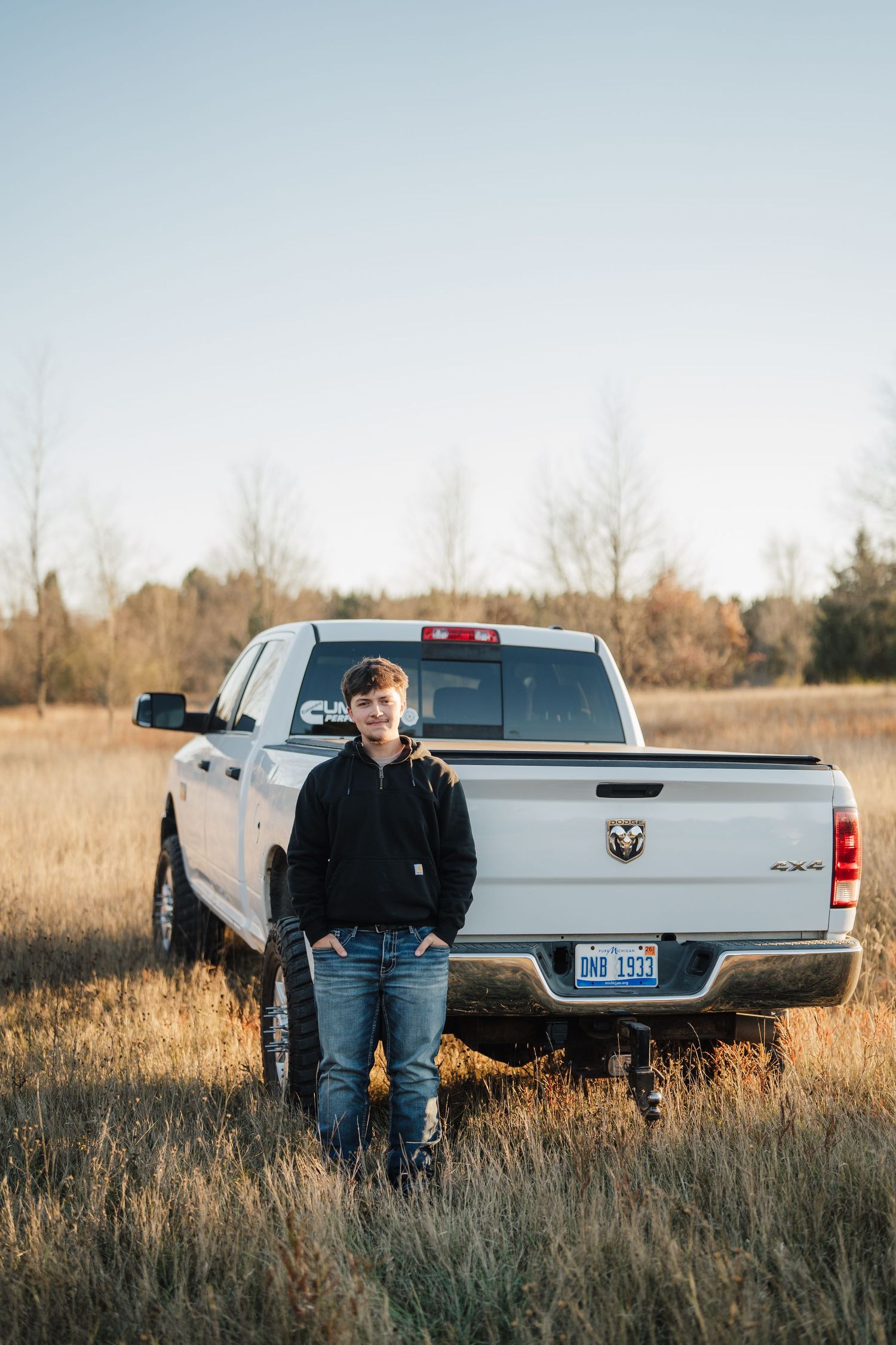A silver Dodge Ram pickup truck parked in a golden field during sunset with tall grass in the foreground.