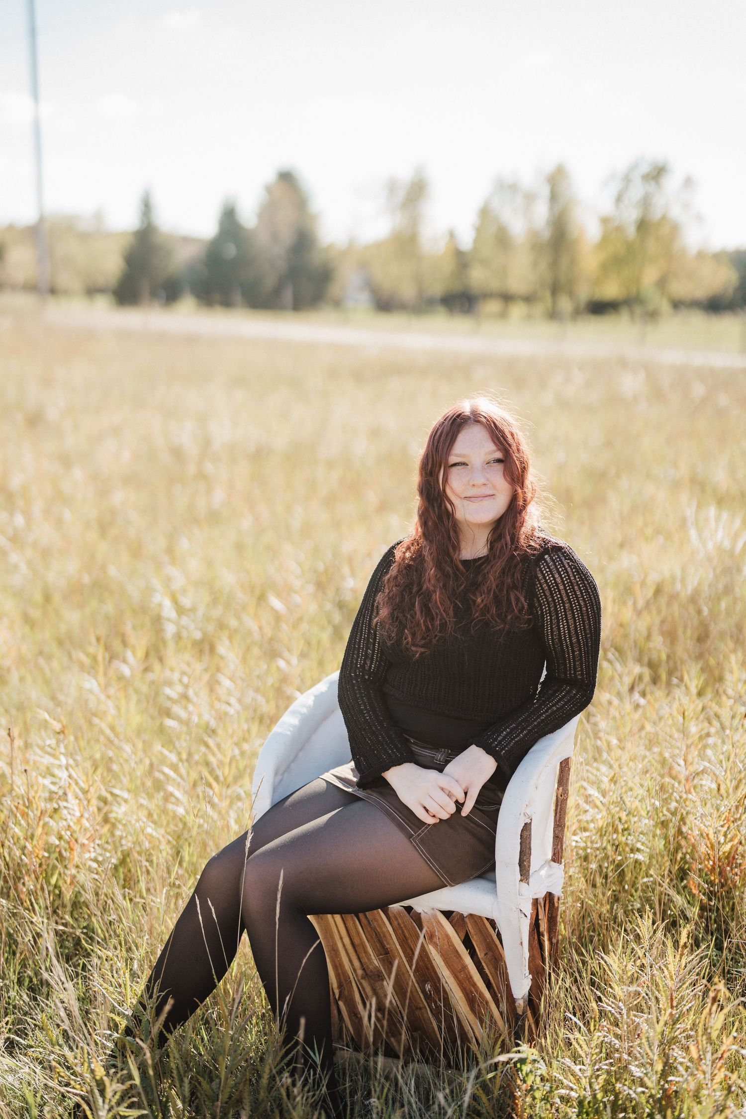 A cozy autumn portrait session in a golden field with a white plastic chair and black knit sweater.