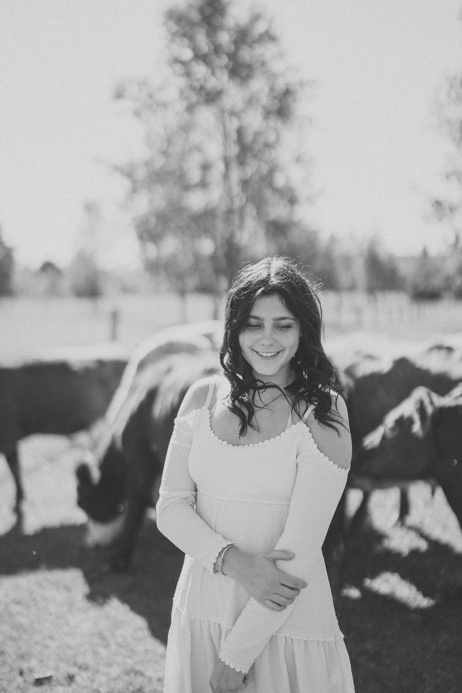 Black and white photo of a person in a white dress standing in a field with cows grazing in the background.