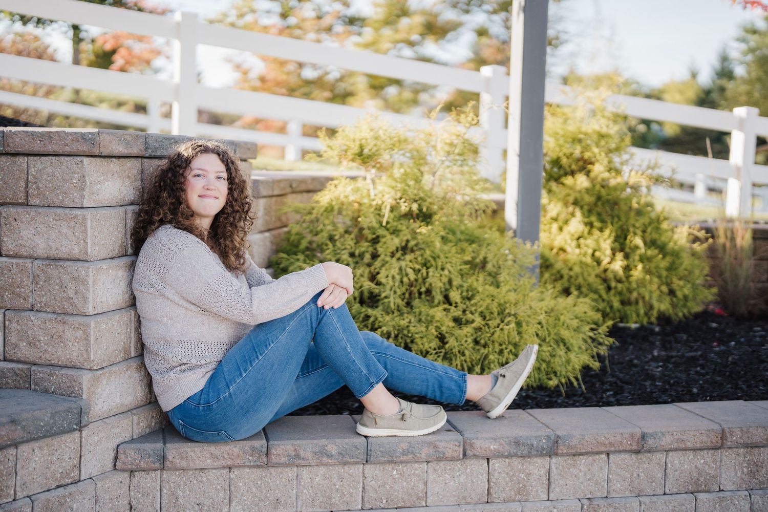 Person in casual attire lounging on outdoor brick wall during golden hour lighting.