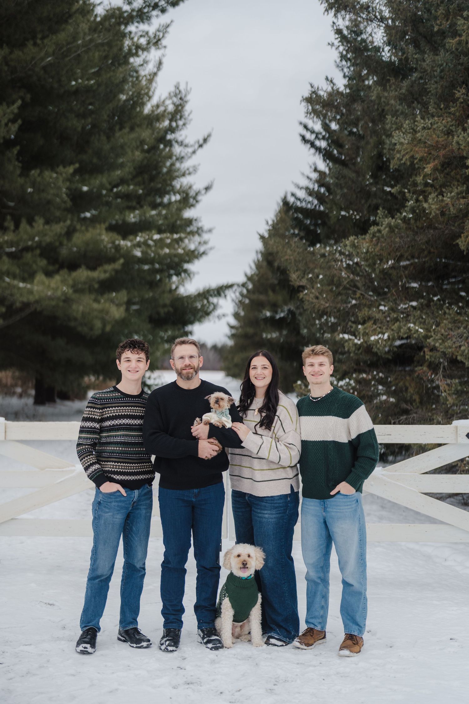 A group stands together in a snowy winter landscape with evergreen trees in the background.