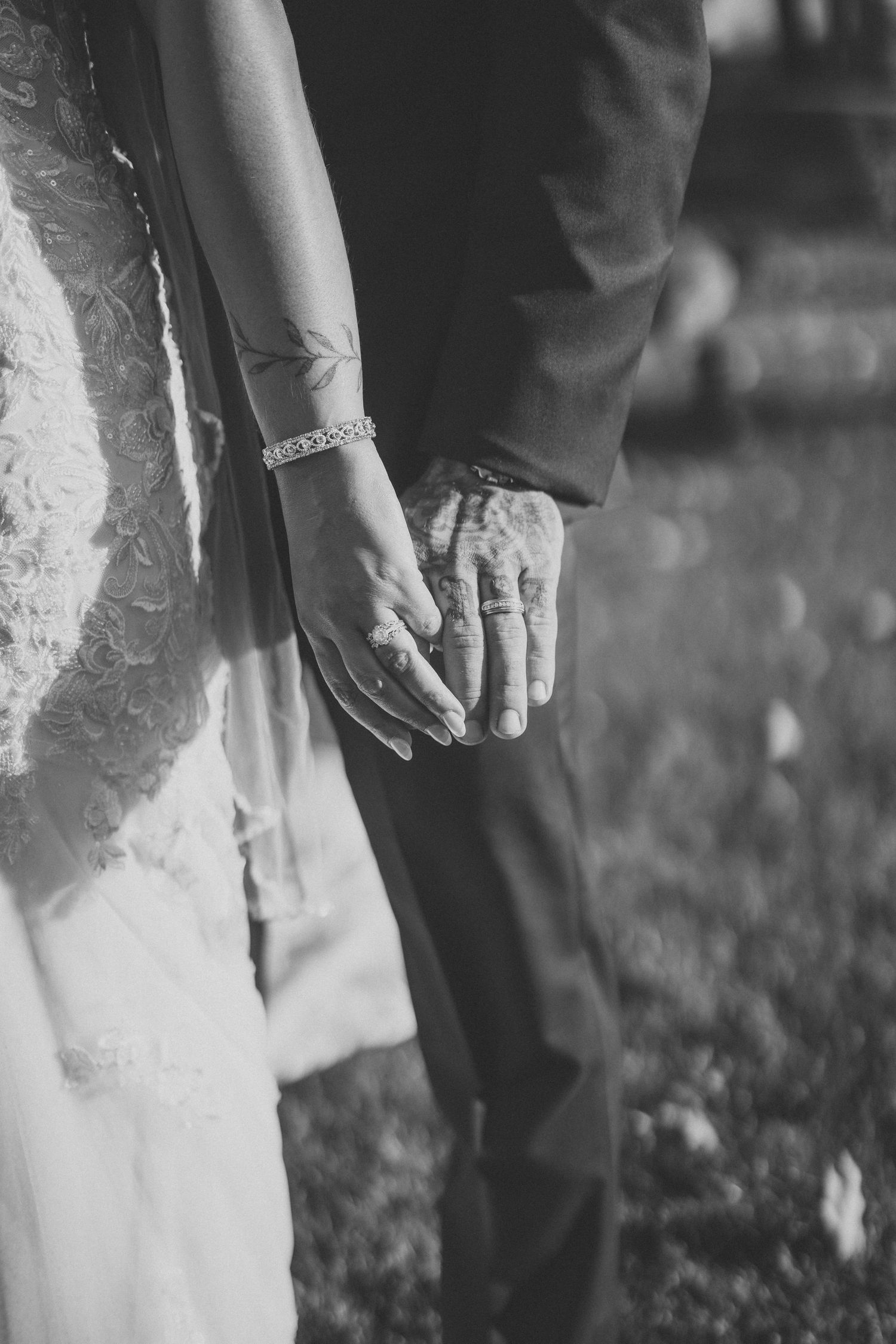 Close-up detail of hands with wedding rings and lace dress during an outdoor ceremony.