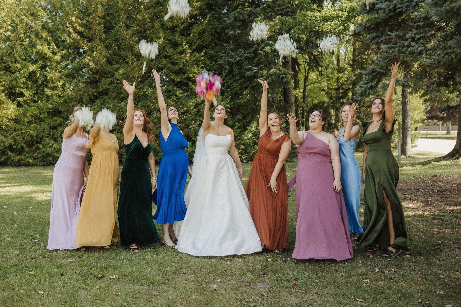 A group in colorful formal attire poses together in a garden setting for an outdoor wedding celebration.