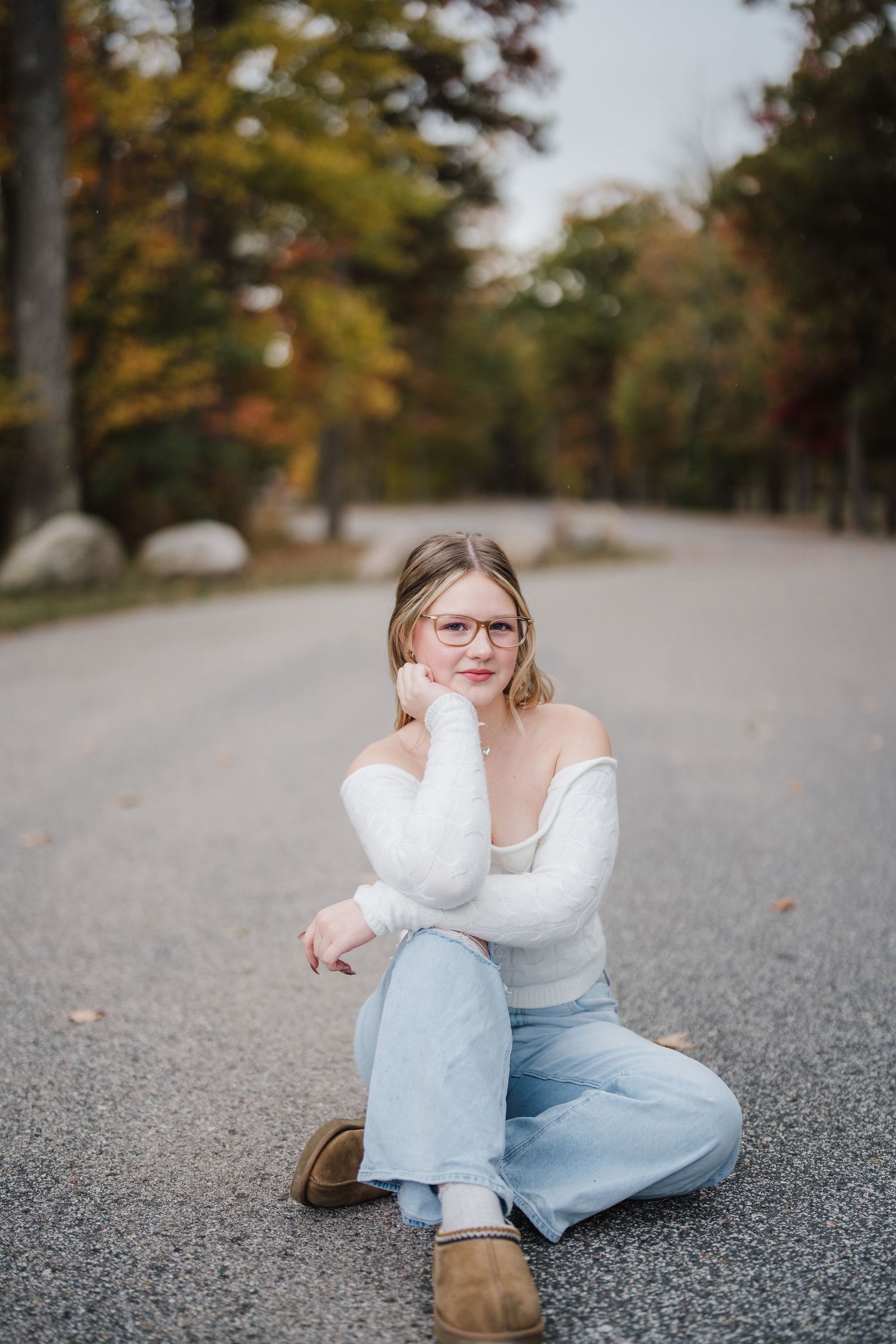 A person in light clothing sits on an autumn road surrounded by colorful fall foliage and trees.