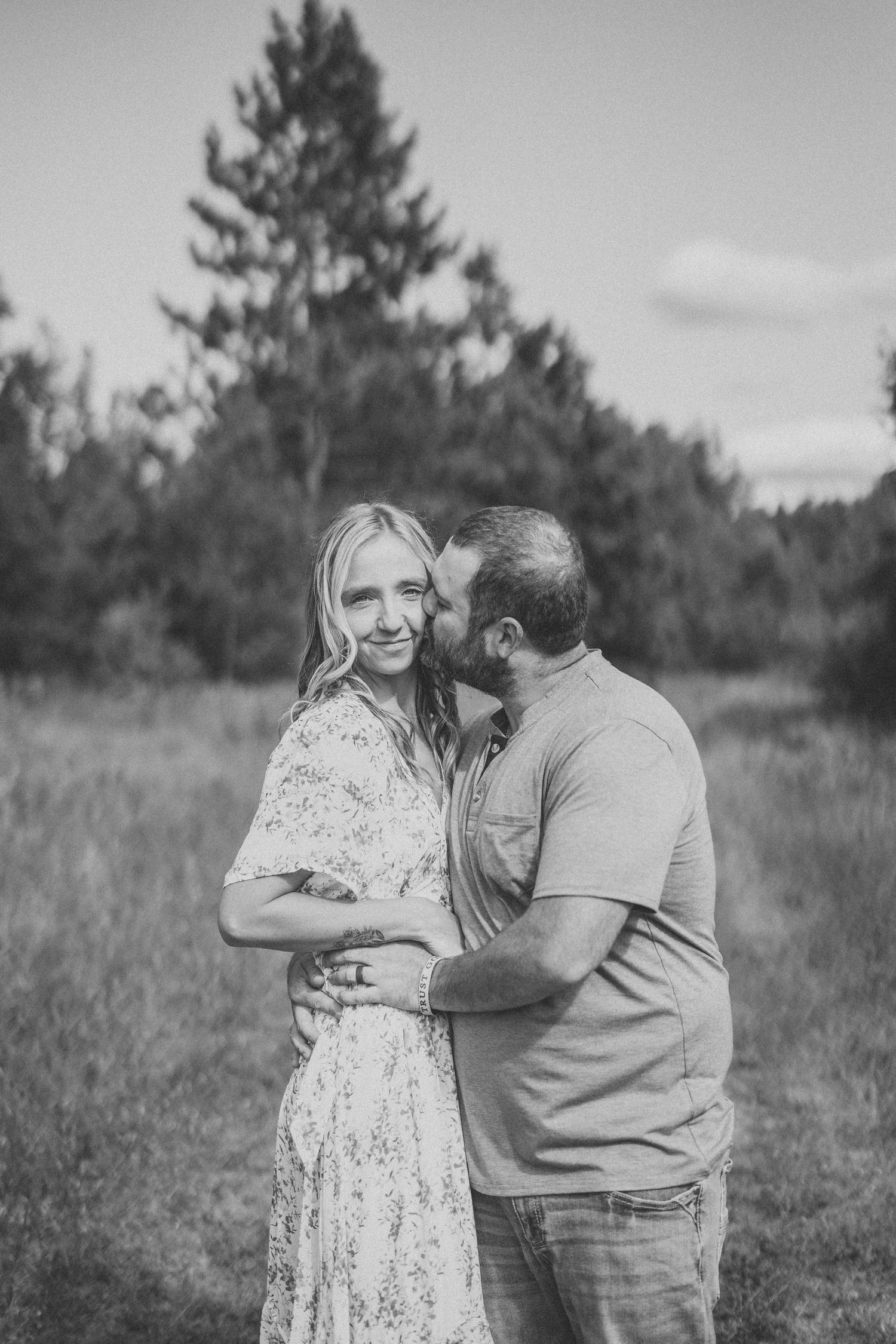 Intimate black and white portrait session in a serene outdoor setting with pine trees in background.