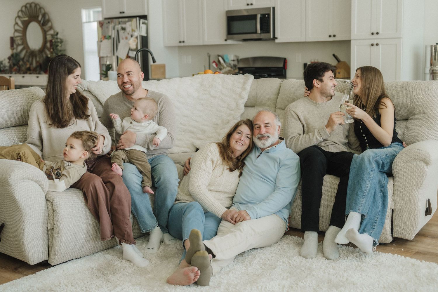 A sequence of four connected images showing a cozy family lounging together on a white couch in a bright living room.