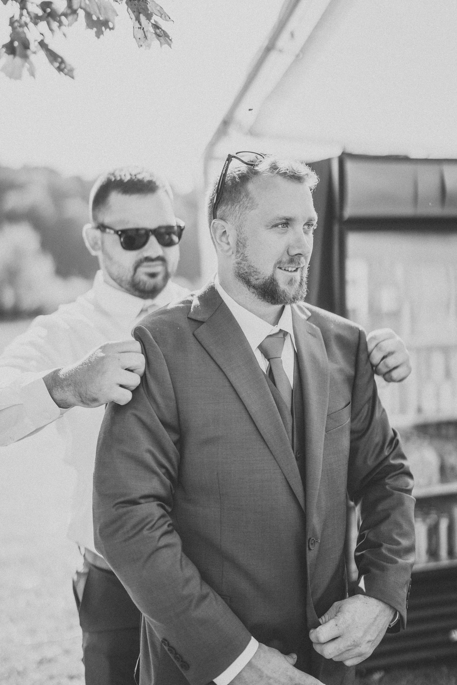 A group of groomsmen in dark suits and sunglasses stand together outdoors in black and white photography.