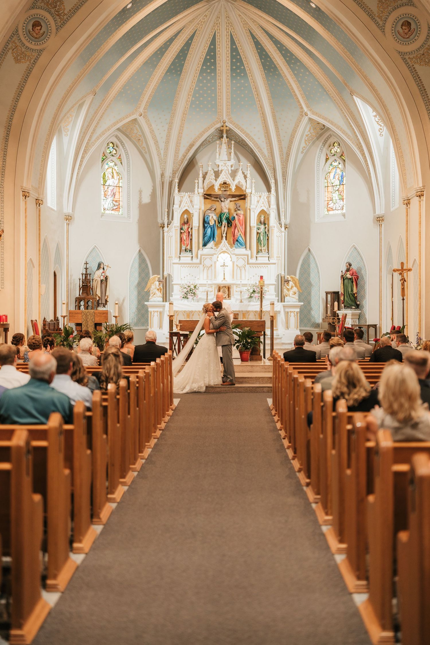 Interior view of a Catholic church during a wedding ceremony with vaulted ceilings and stained glass windows.
