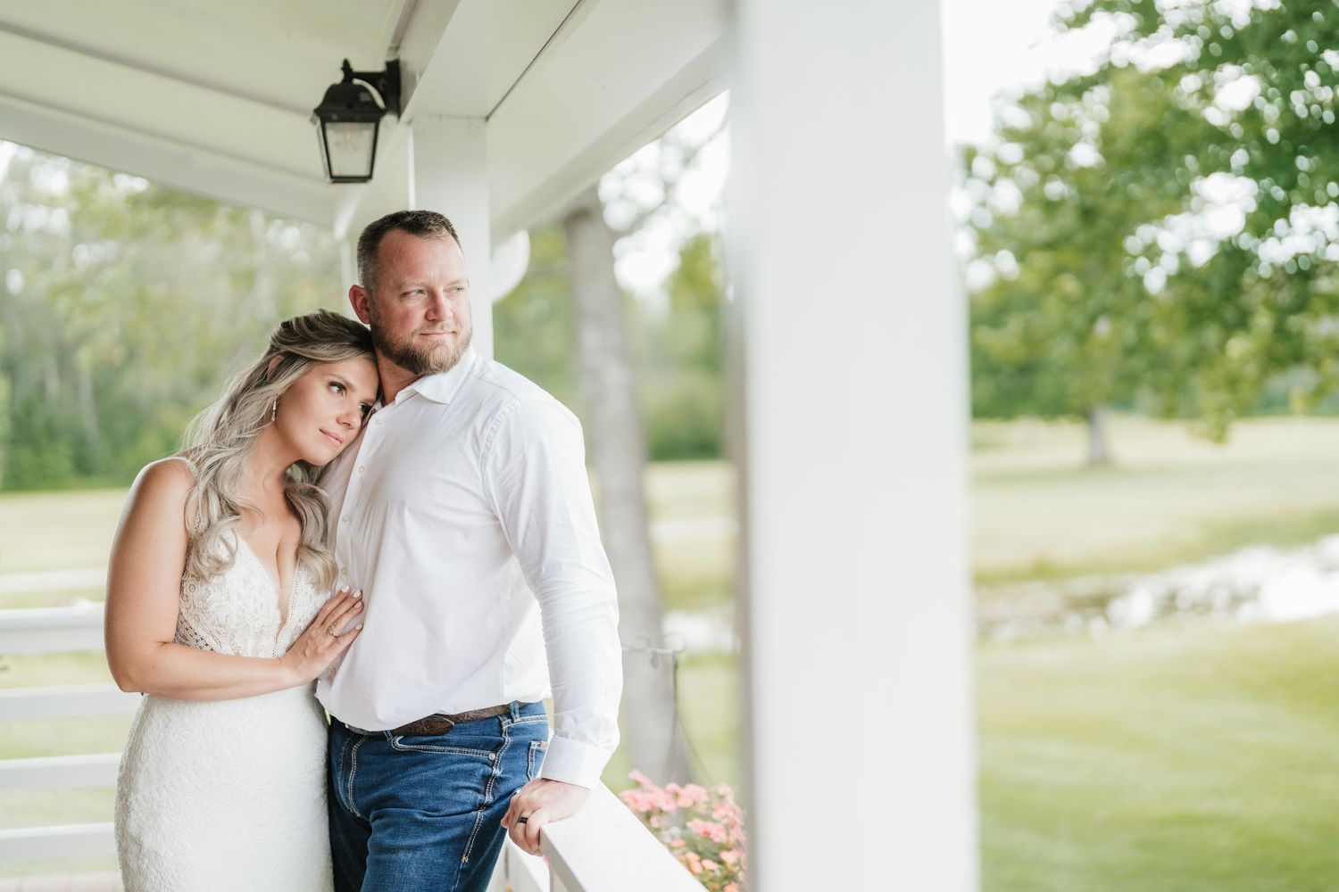 Couple embraces on white porch during romantic countryside wedding photoshoot.