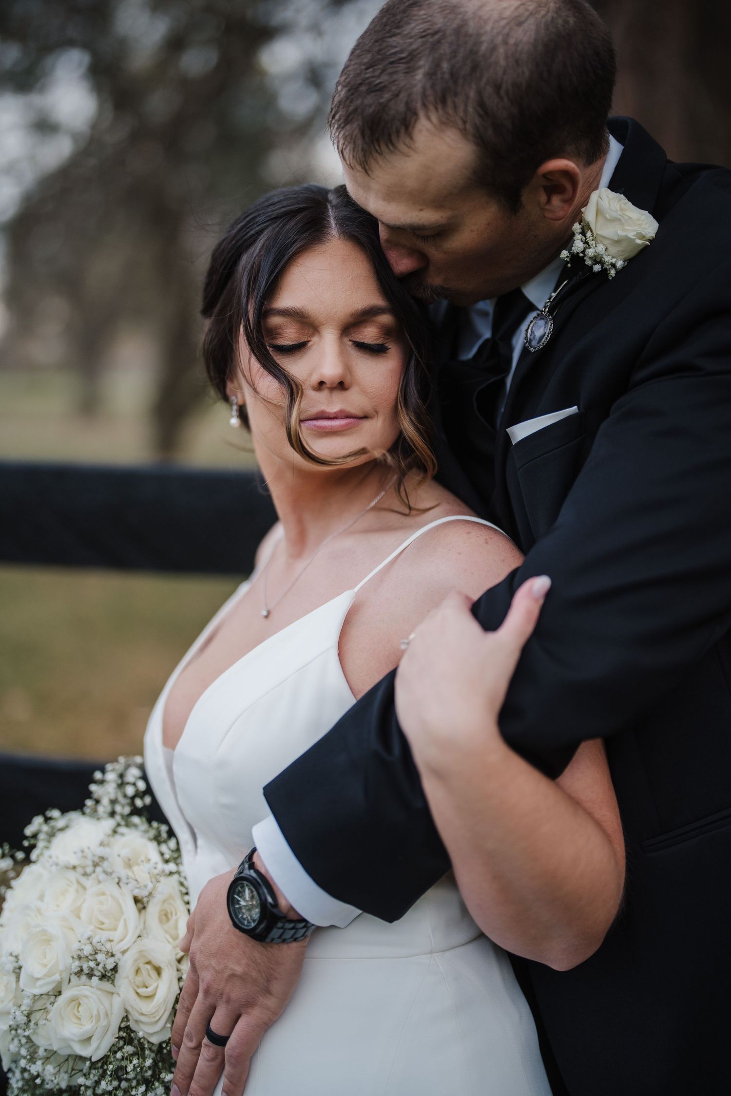 Intimate wedding portrait of a couple embracing outdoors with white rose bouquet.