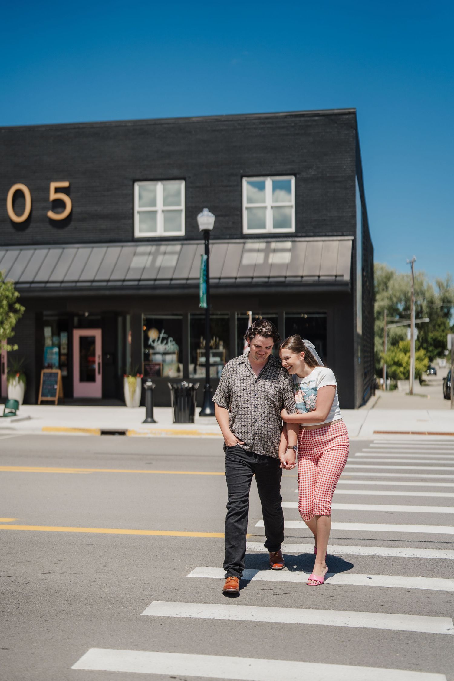 A couple walks together across a crosswalk in front of modern black commercial buildings on a sunny day.