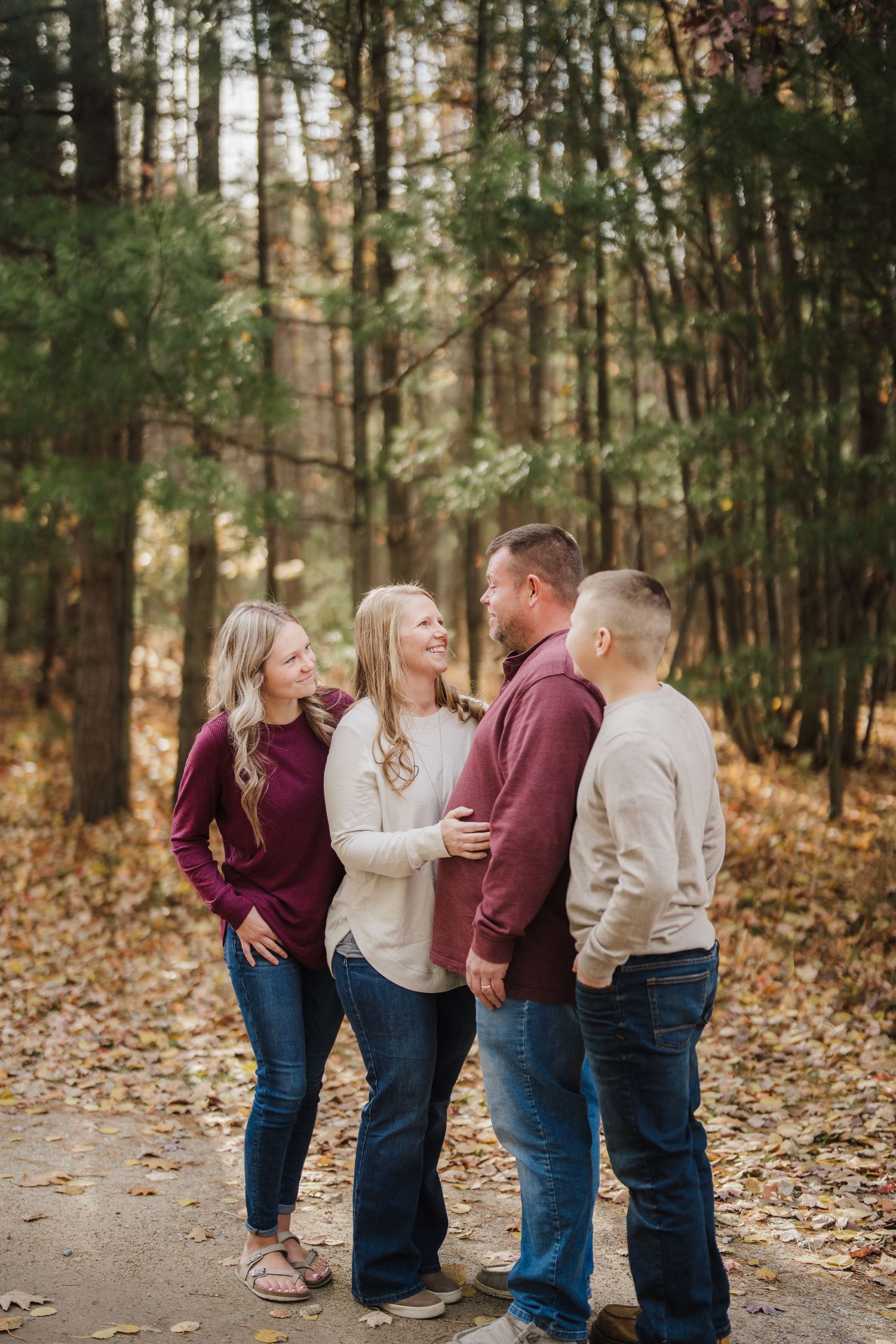 A family wearing coordinated burgundy and cream outfits shares candid moments together in a wooded autumn setting.
