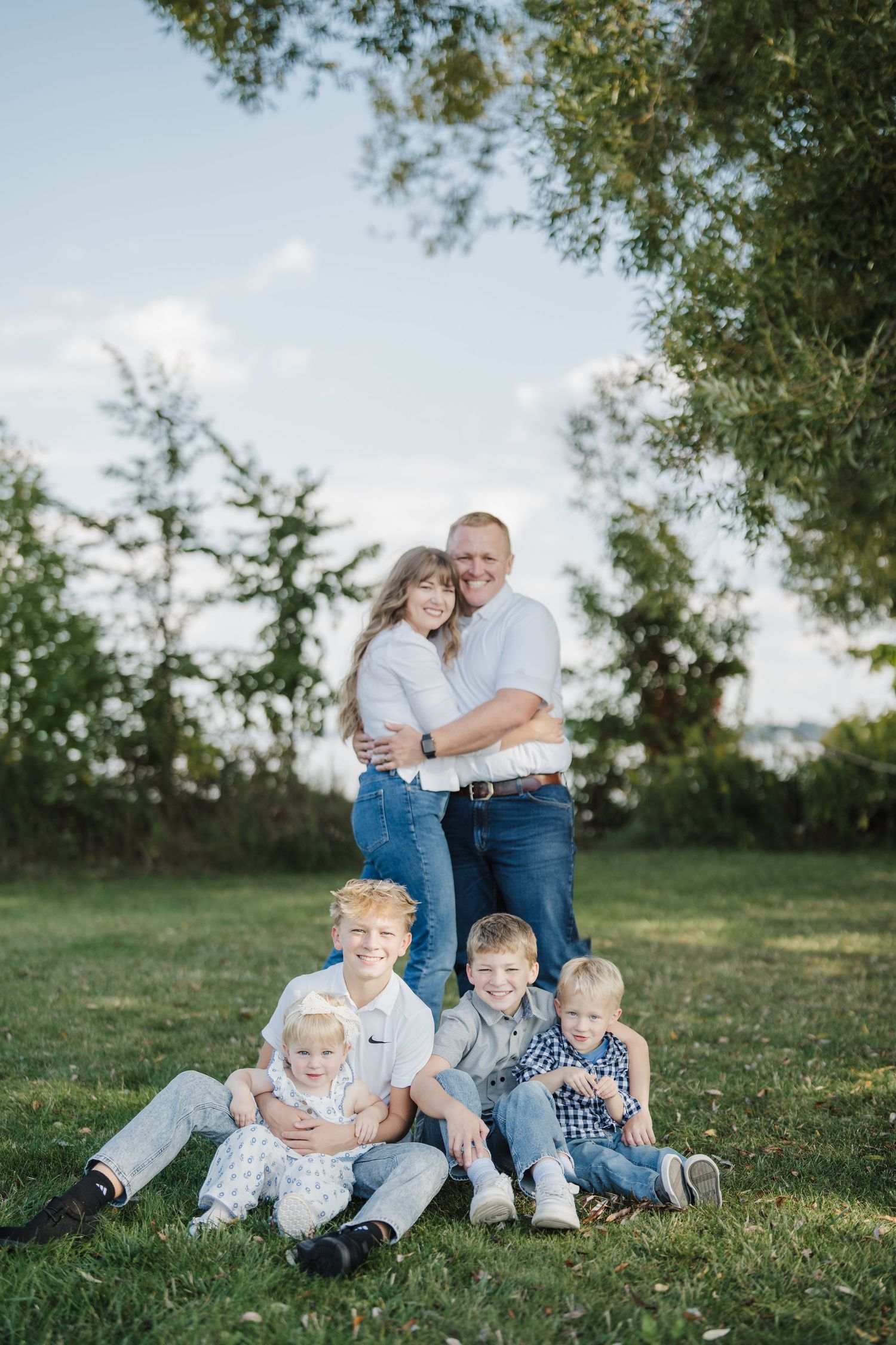 A family relaxes together on green grass during an outdoor photo session on a sunny day.
