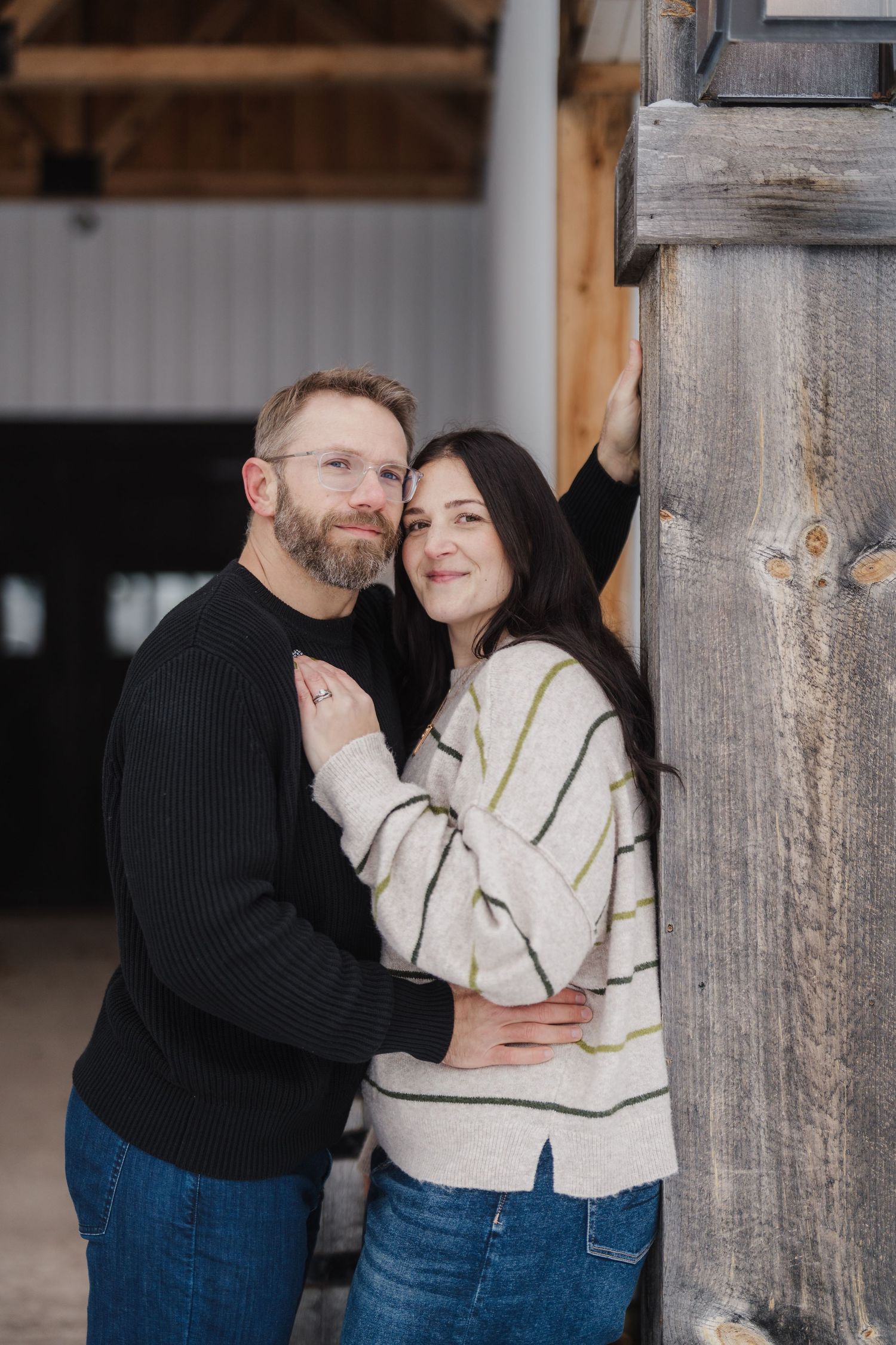 A couple embraces in a rustic barn doorway wearing matching knit sweaters and denim.
