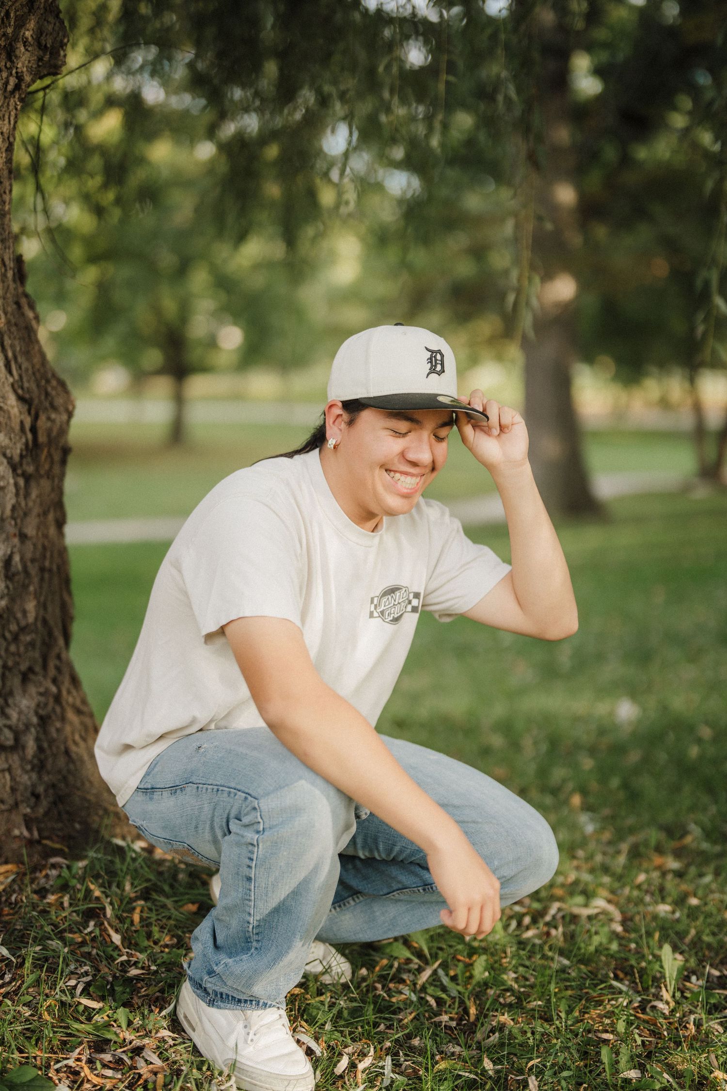 Person in white t-shirt, jeans and Detroit baseball cap crouches in a grassy outdoor setting.