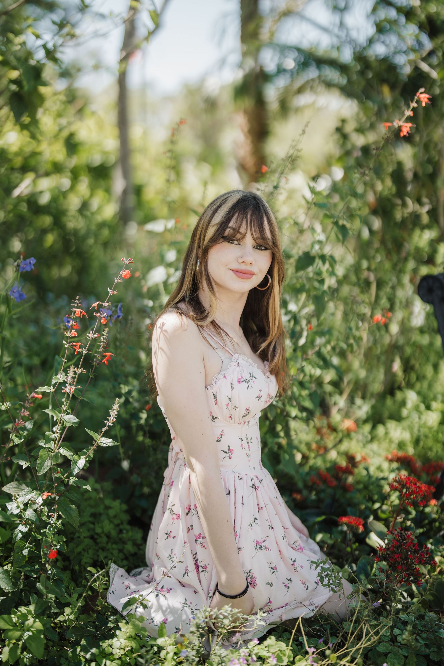 A delicate floral dress stands out against lush greenery and blooming flowers in a garden setting.
