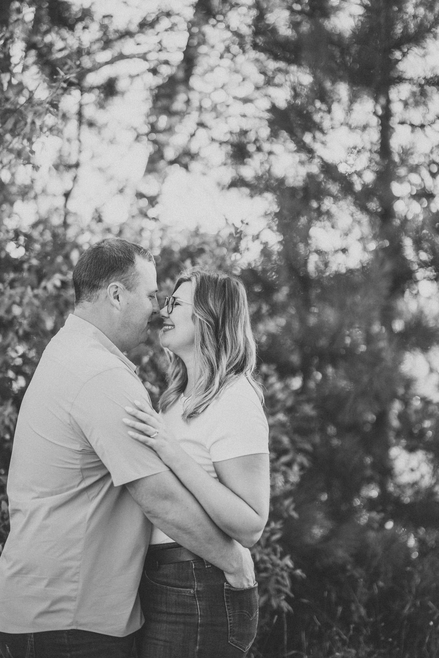 A romantic couple shares tender moments in a series of black and white photos taken outdoors against a sunlit forest backdrop.
