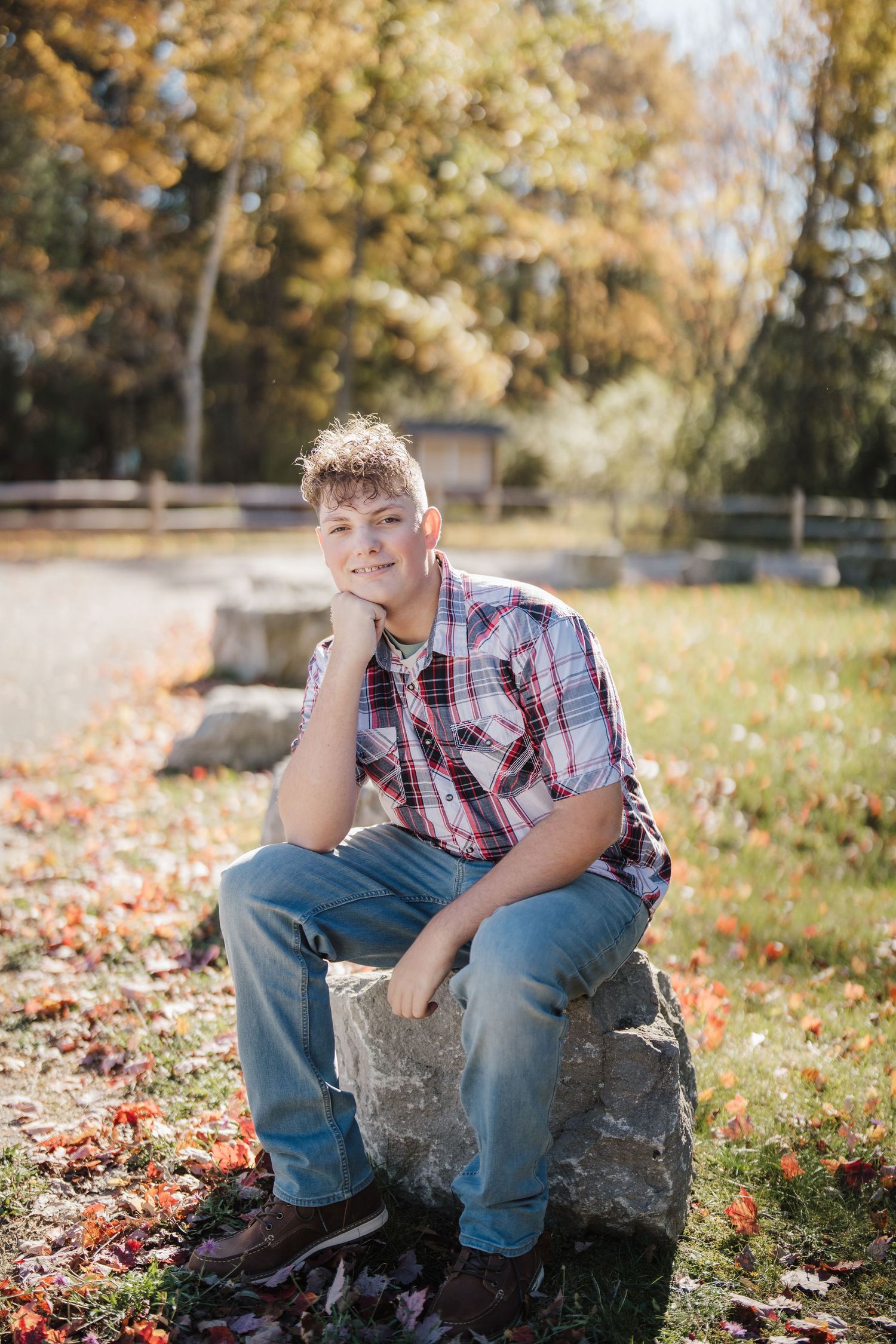 Casual outdoor photo shoot on a rock surrounded by autumn leaves and golden sunlight.
