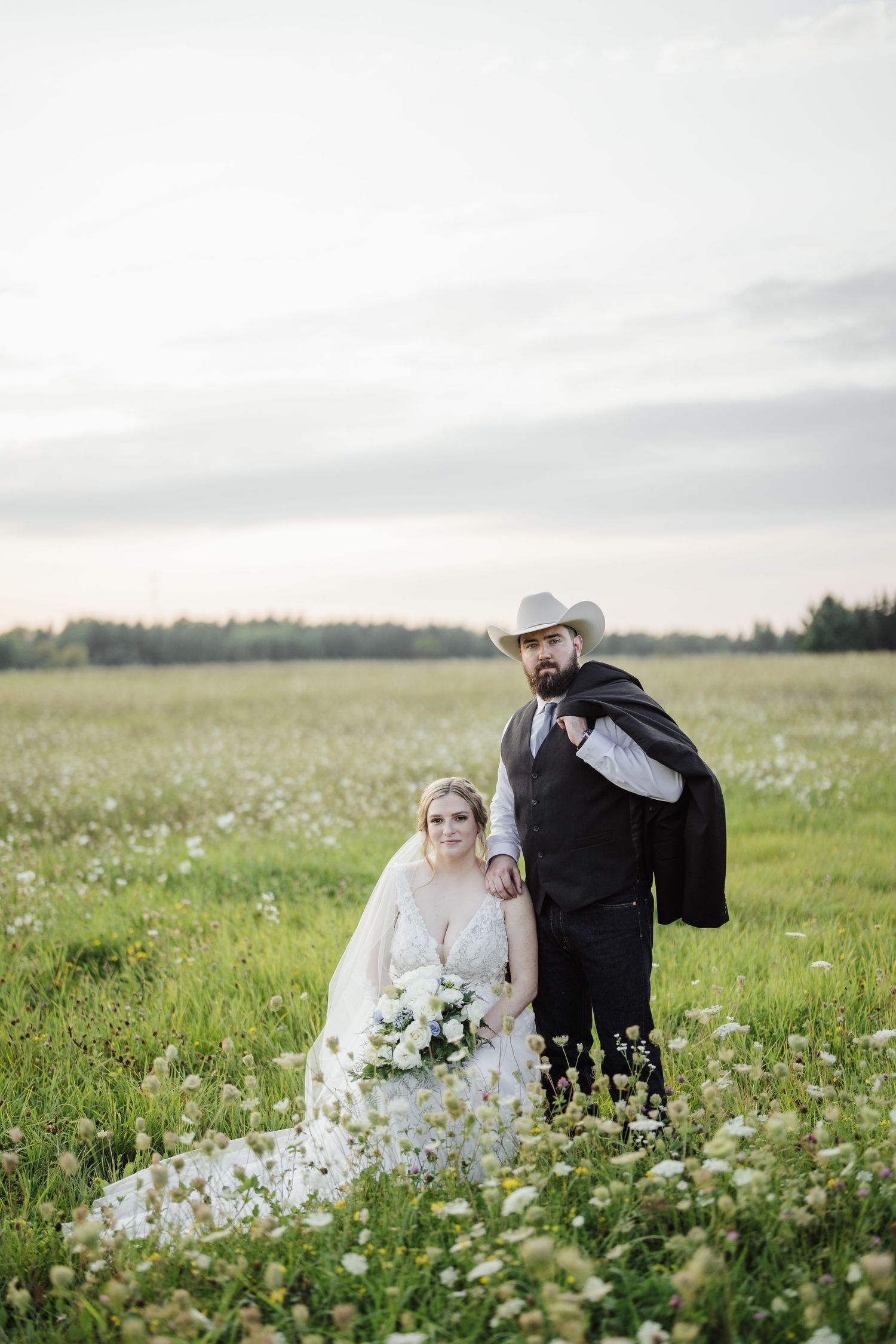 Wedding couple stands in wildflower meadow with mountain forest backdrop.