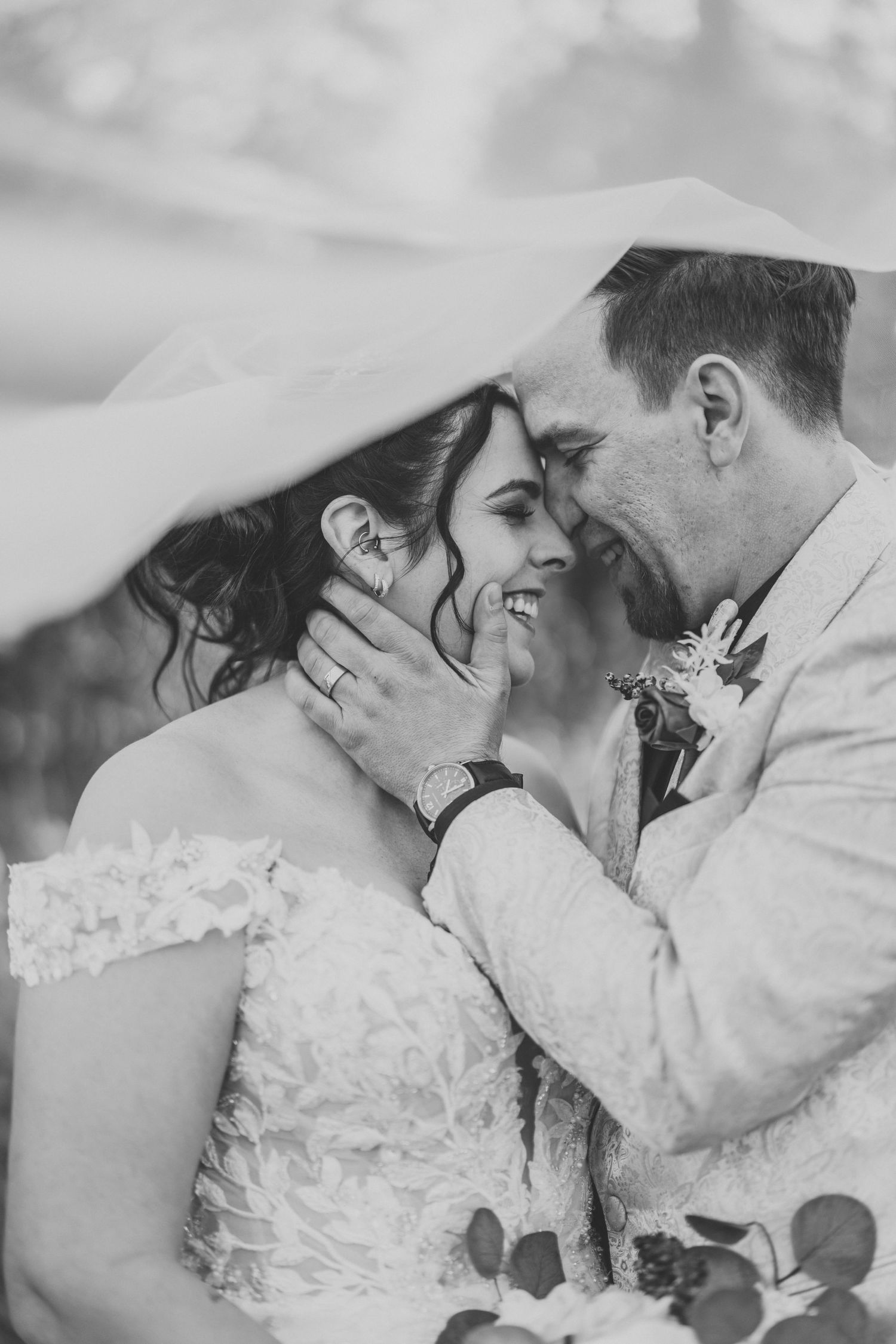 Black and white intimate portrait of wedding couple sharing tender moment under veil.