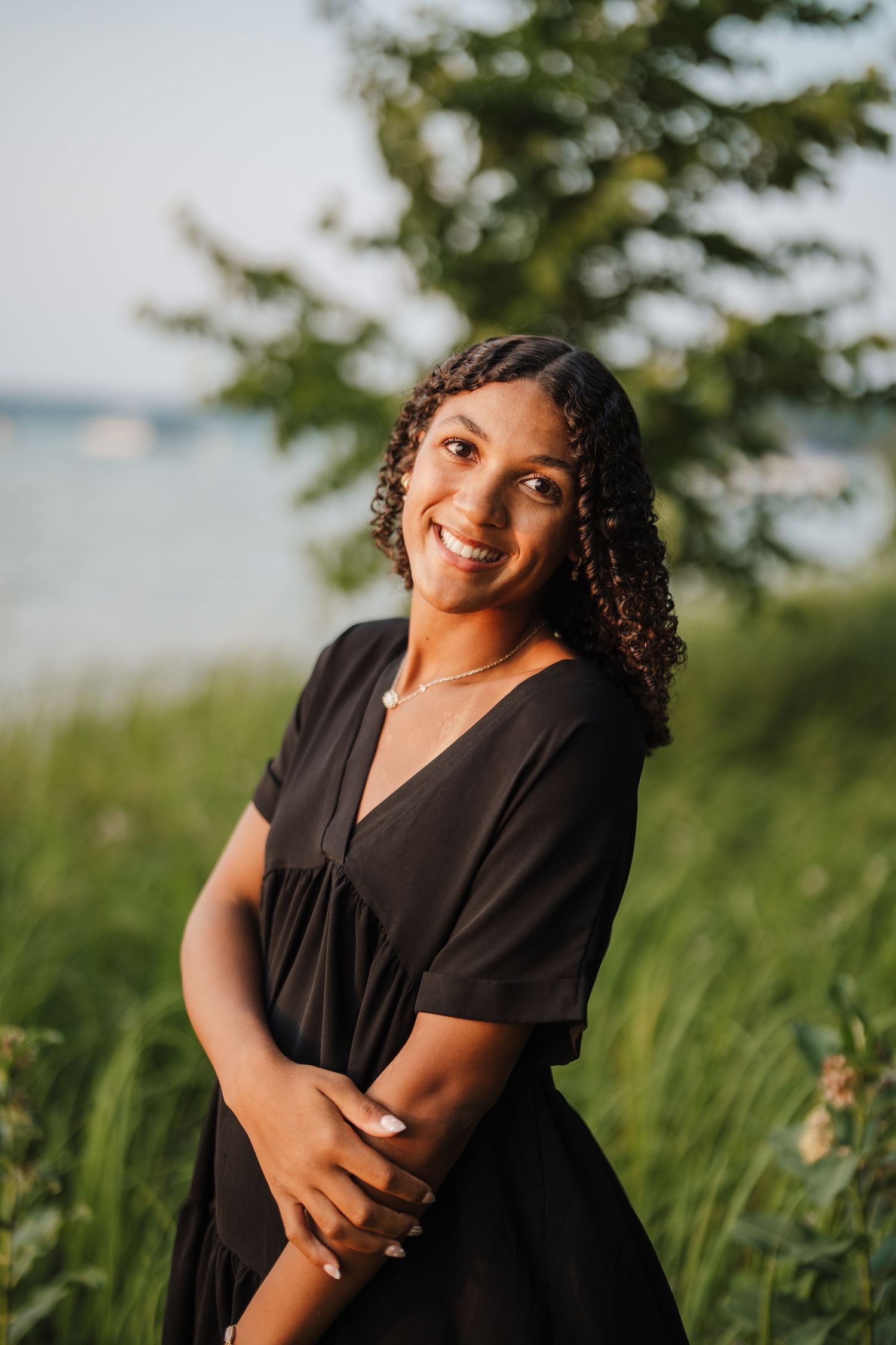 A summer portrait in a black dress against a waterfront background with trees and natural lighting.