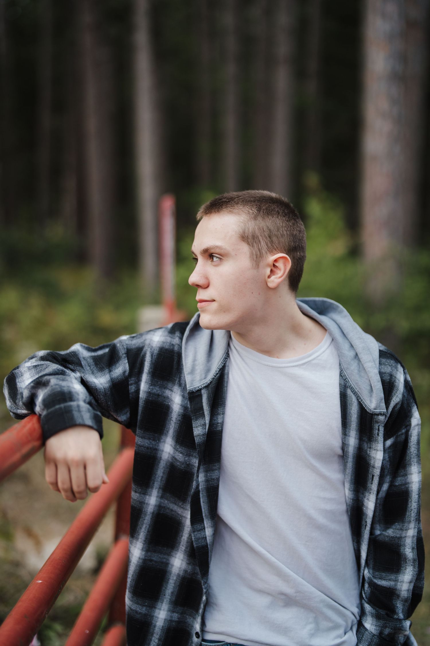 Person wearing plaid flannel shirt and white t-shirt poses against forest backdrop in artistic series.