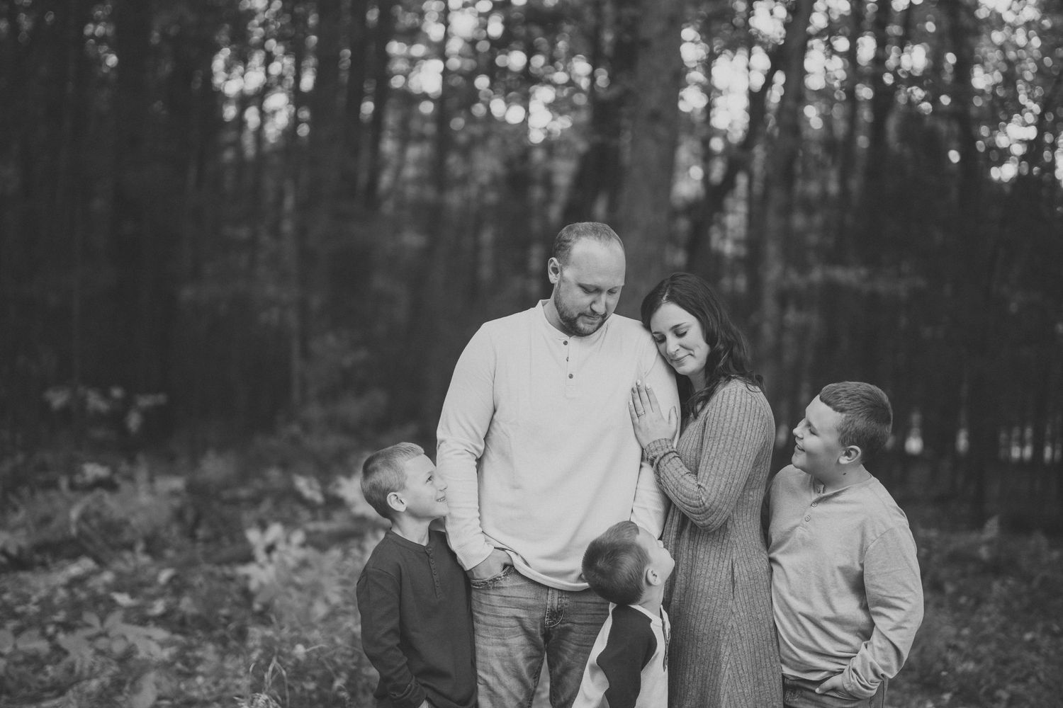 A series of black and white photos showing a couple embracing in a wooded outdoor setting during a romantic photoshoot.