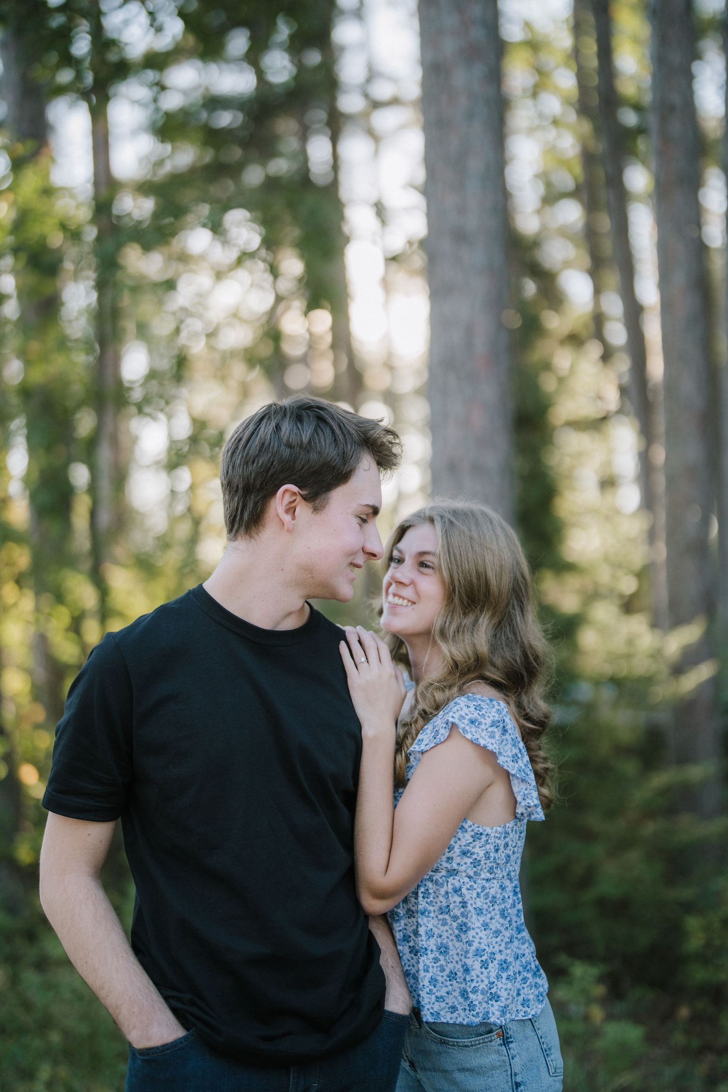A couple shares an intimate moment together in a sunlit forest setting, wearing casual clothes.