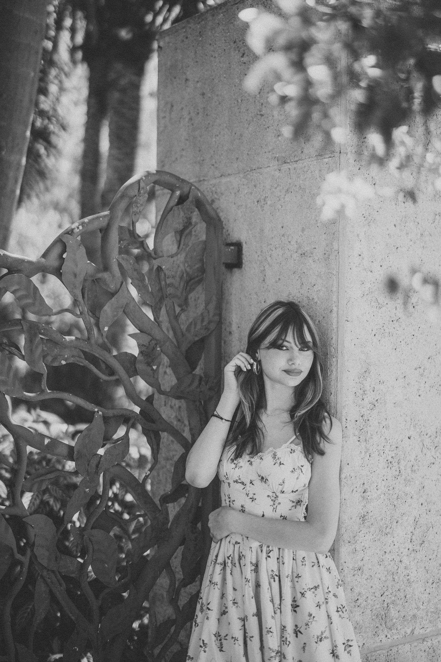 A dreamy black and white portrait in a floral sundress against a textured wall with natural foliage.