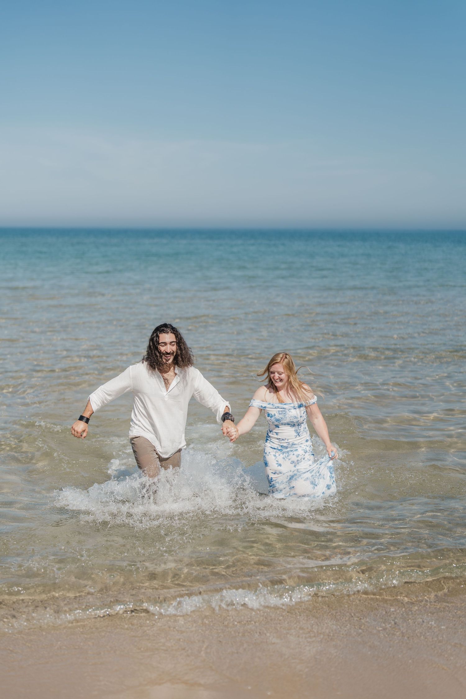 A couple splashes and plays together in the shallow ocean waves on a bright summer day.