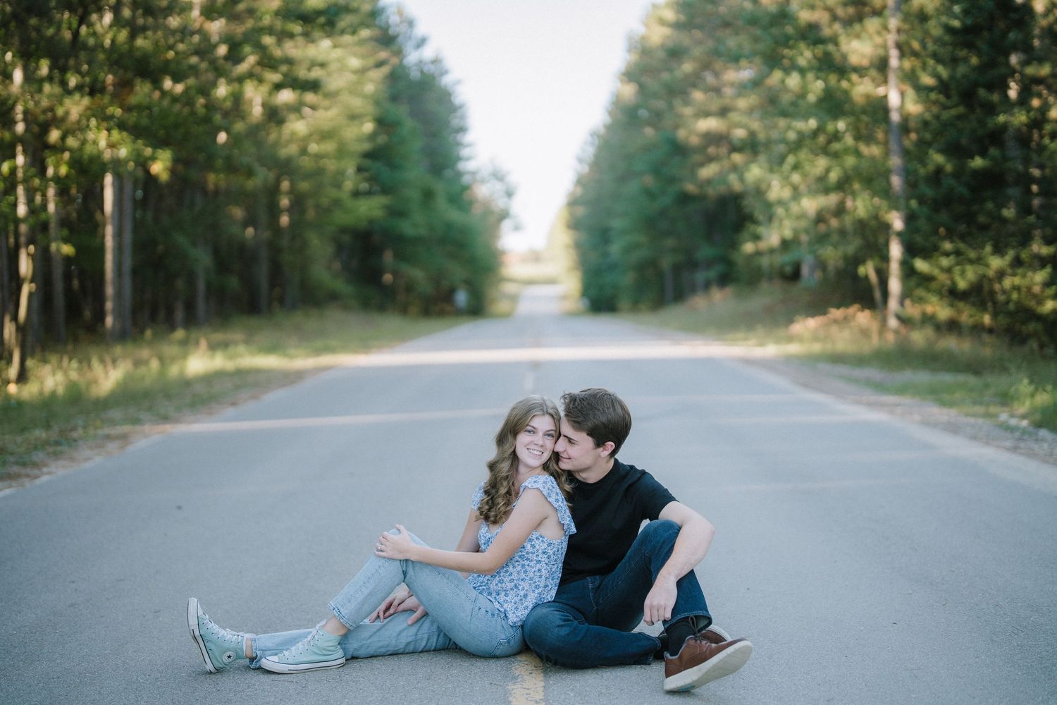 Two people lying on an empty forest road while sharing an intimate moment at sunset.