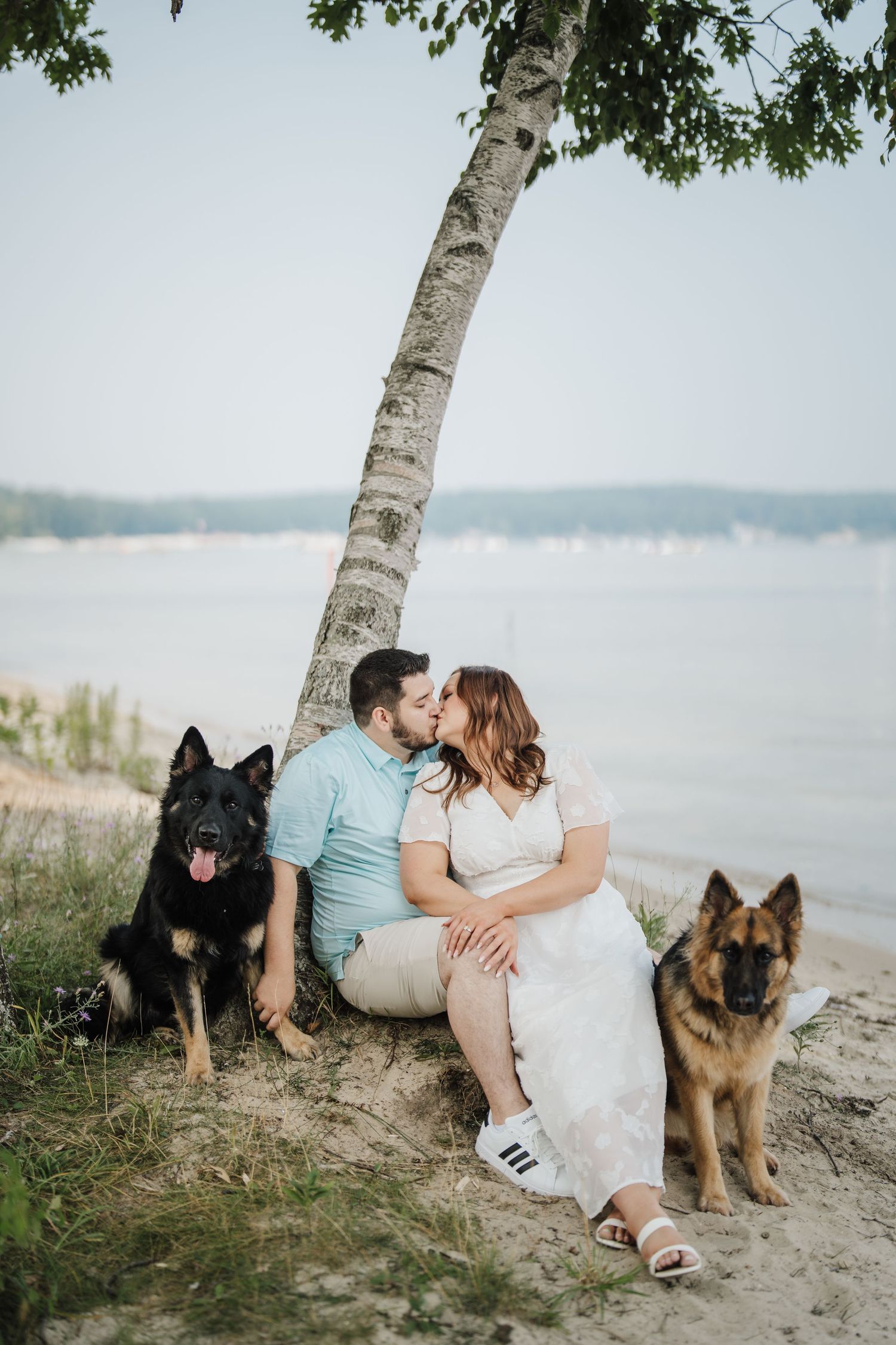 A couple sits on a beach with their German Shepherd dogs beside them during a romantic outdoor photo session.