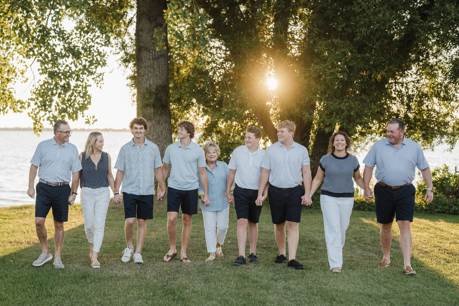 Group of people walking together on grass during golden hour sunset with trees in background.