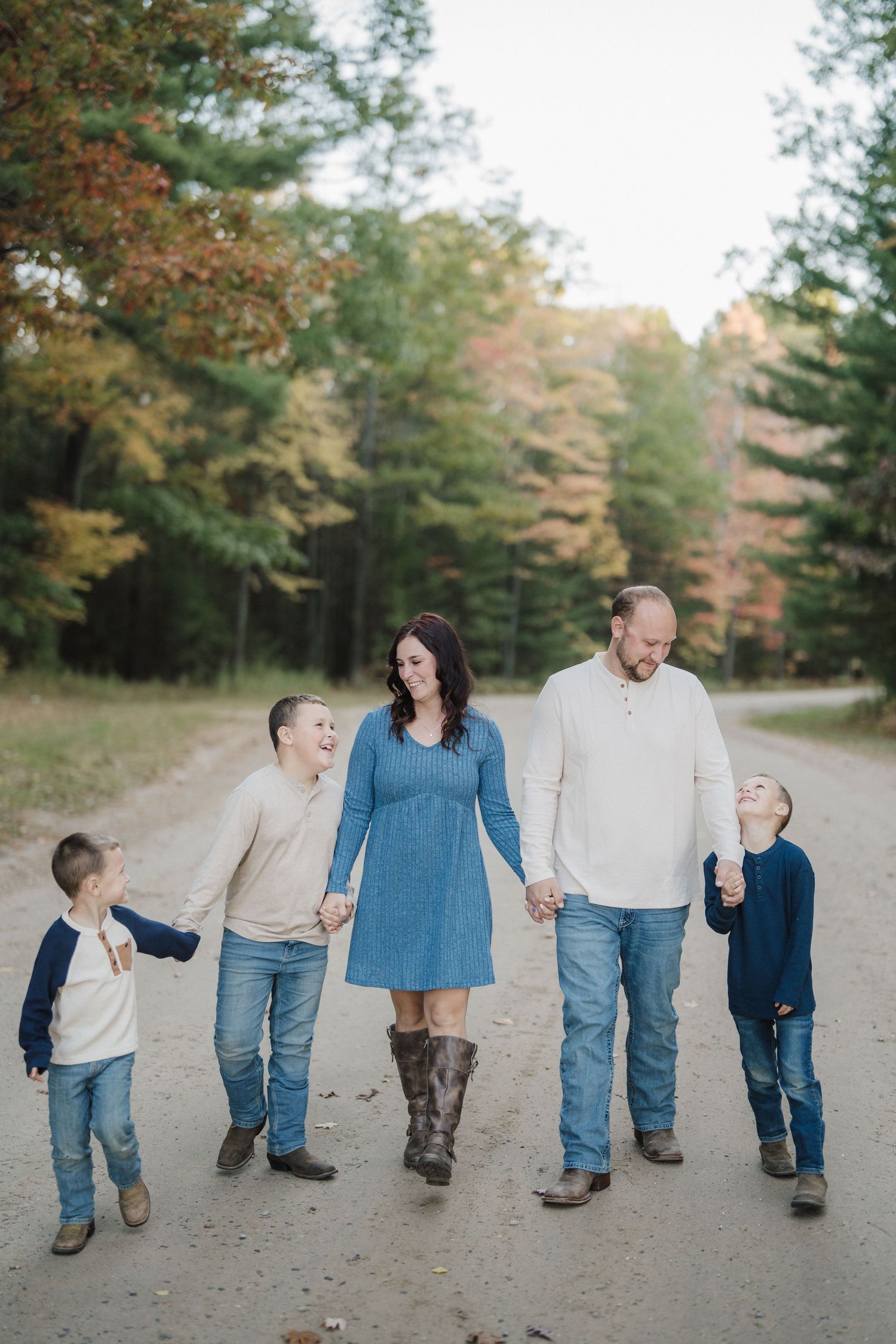 A family walks together on a dirt road surrounded by autumn trees with changing fall foliage colors.