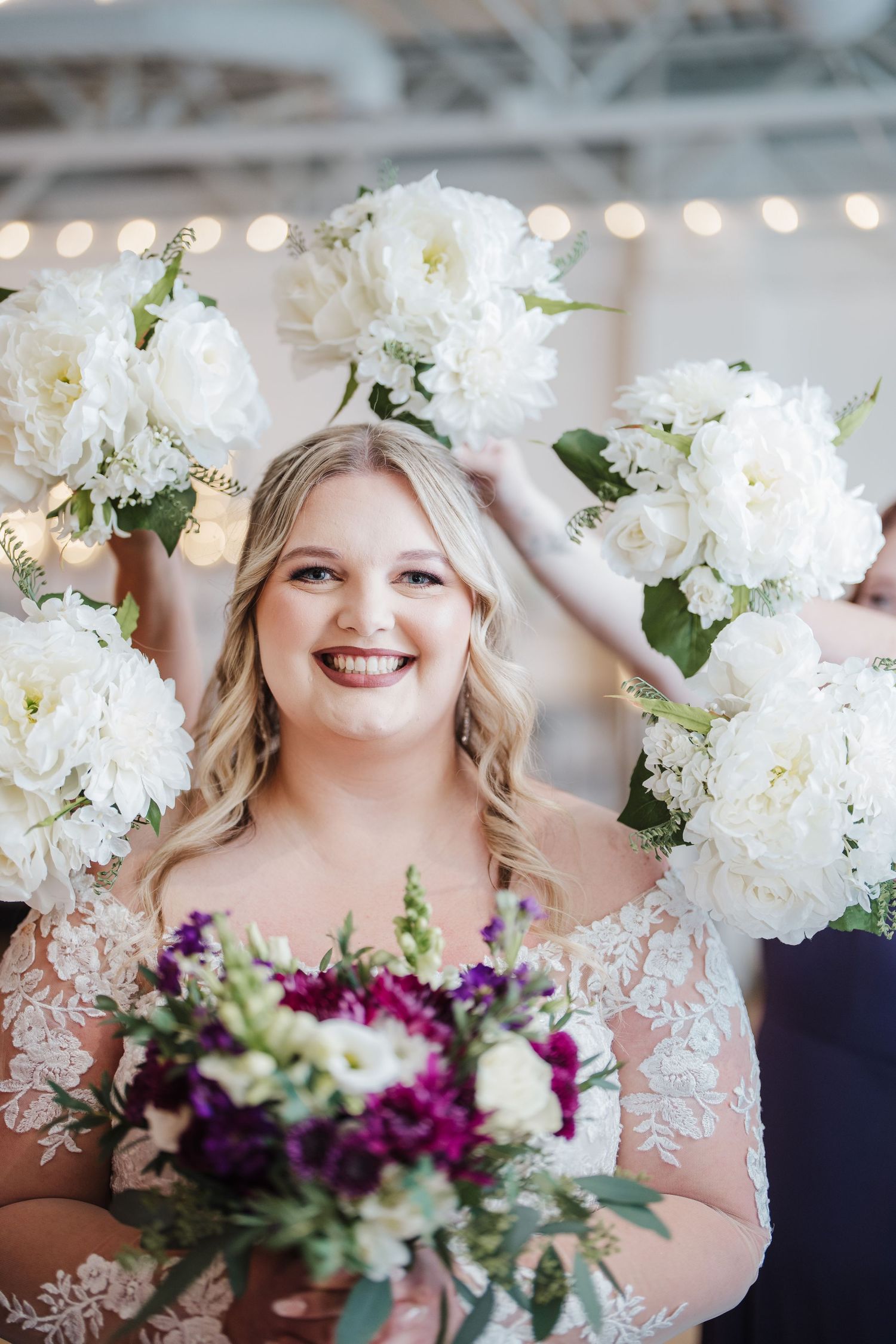 A bridal portrait surrounded by white floral arrangements and holding a vibrant purple bouquet.